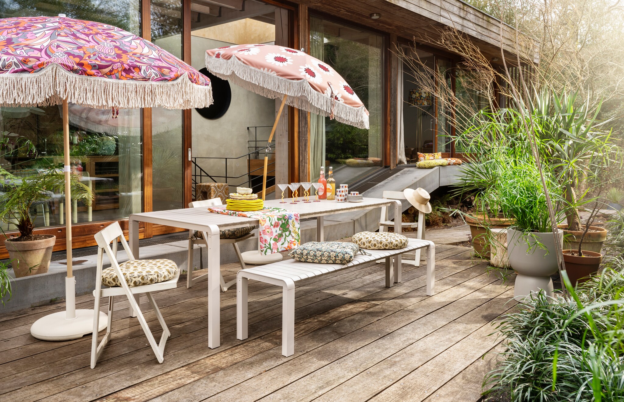 Metalen tuintafel Vondel van Zuiver, 214x94x75 cm (bxdxh) € 1299,-, metalen tuinbank Vondel van Zuiver, 175x45x45 cm (bxdxh) € 749,-, bloempot Pure Coupe van Elho, gerecycled kunststof, 35x49 cm (Øxh) € 105,-, kussen Bloom van HKliving, gerecycled pet, 35x60 cm € 27,99 (vtwonen.nl/shop). Parasol Tropical Flowers en parasol Floral Beige, gerecyclede plastic flessen, 180 cm (Ø) per stuk € 159,95 (embellish-living.nl). Betonnen parasolvoet Sora € 29,- (kwantum.nl). Rond katoenen matraskussen van Madam Stoltz, 40 cm (Ø) € 20,-, katoenen matraskussen Madam Stoltz € 20,- (deens.nl). Houten klapstoelen van Aldo Jacober € 75,- (whoppah.com). Gele porseleinen dinerborden Perle, set van 2 € 35,- (klevering.com). Roze keramieken dinerborden Bloem € 7,99 (xenos.nl). Glazen coupes Curve van &amp;Klevering, set van 2 € 45,- (groenenakker.nl). Keramieken schaal Mimosa € 14,99 (bloomingville.com). Katoenen tafelkleed € 24,95 (hm.com). Wit gebloemd keramieken servies vanaf € 0,45 (dekringloper.nl). Katoenen kussen Marigold, 60 cm (Ø) € 74,95, katoenen kussen Daisy, 60 cm (Ø) € 74,95 (hkliving.com). Overig privébezit. vtwonen 06-2024 | styling Kelly van Gendt | fotografie Stan Koolen