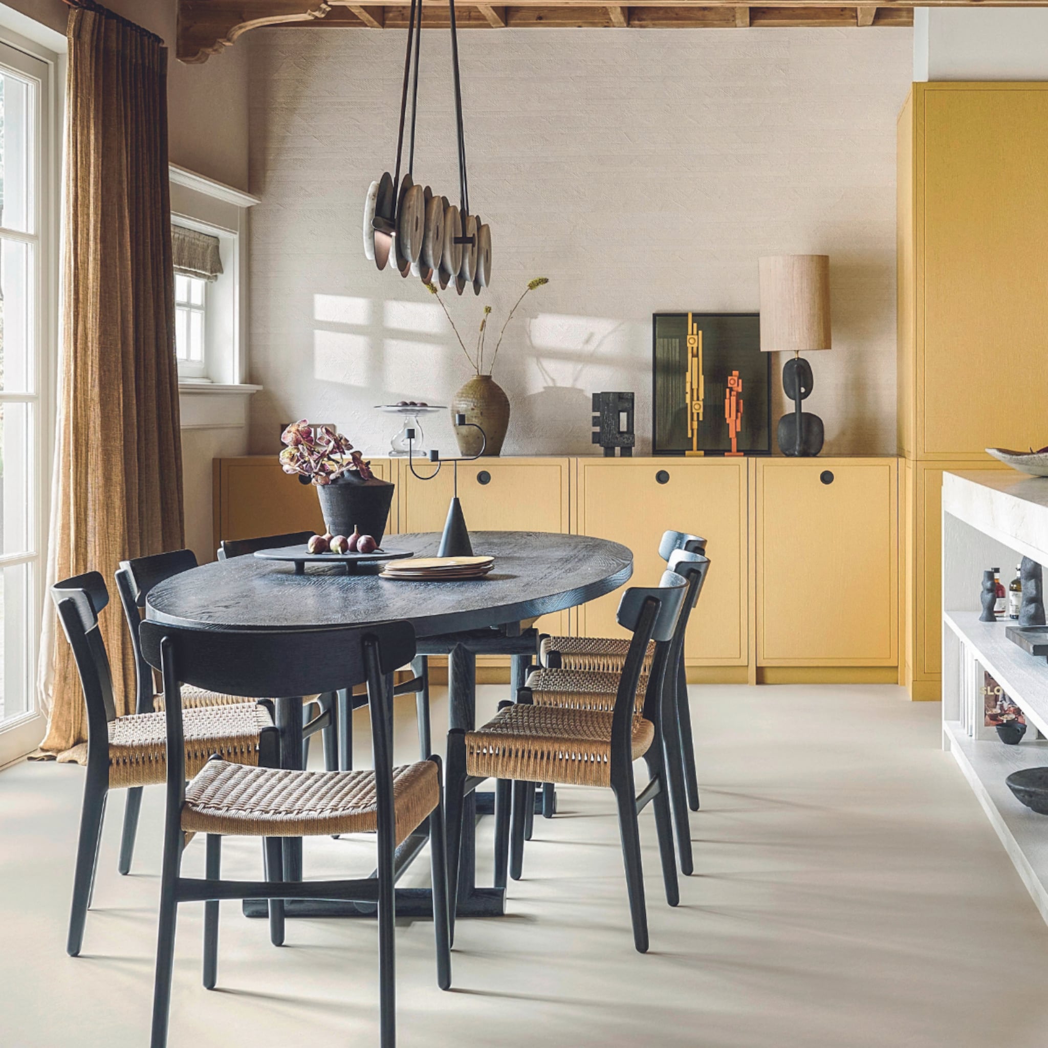 Ovale zwarte eettafel met zwart riete stoelen en gele wandkasten