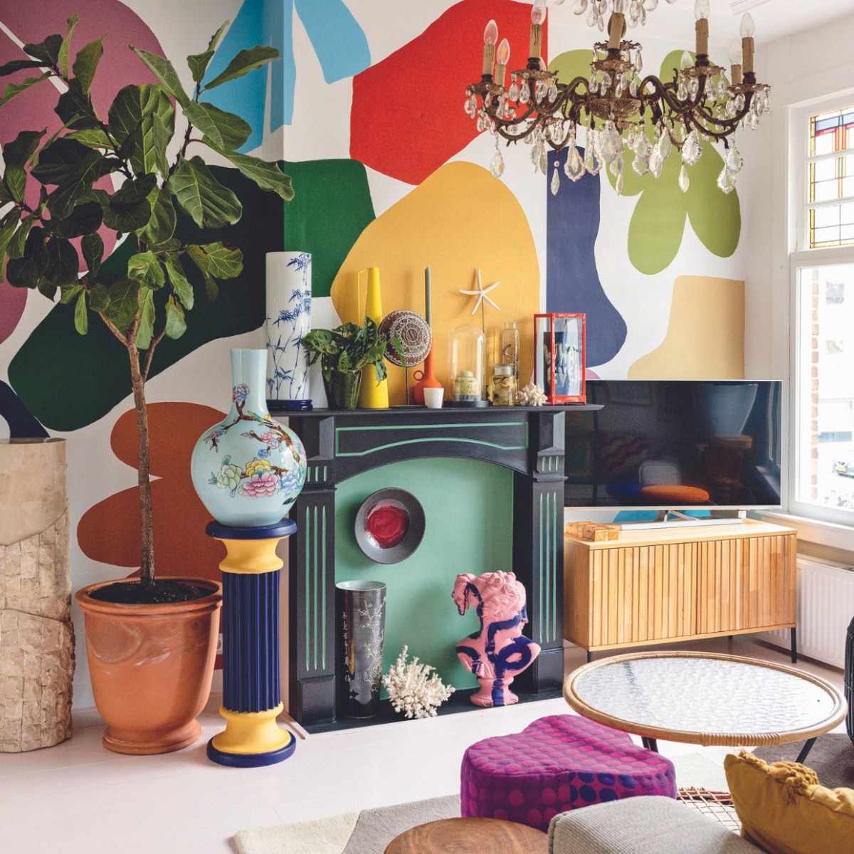 Marmeren zuil en zelf geschilderde pilaar Marktplaats. Terracottapot tuincentrum. Gebloemde vaas, gele vaas, oranje kandelaar, poef en houten bijzettafel Polspotten. Lamp vintage. Vitrinekast, donkere vaas, koraal en bijzettafel met glazen blad kringloopwinkel. Blauwe vaas gemaakt door Sharvin, tv-meubel Woood, bord Norman Trapman, plant Marvy Green. Overig onbekend. vtwonen 04-2024 | styling Ilona Jongepier | fotografie Dana van Leeuwen