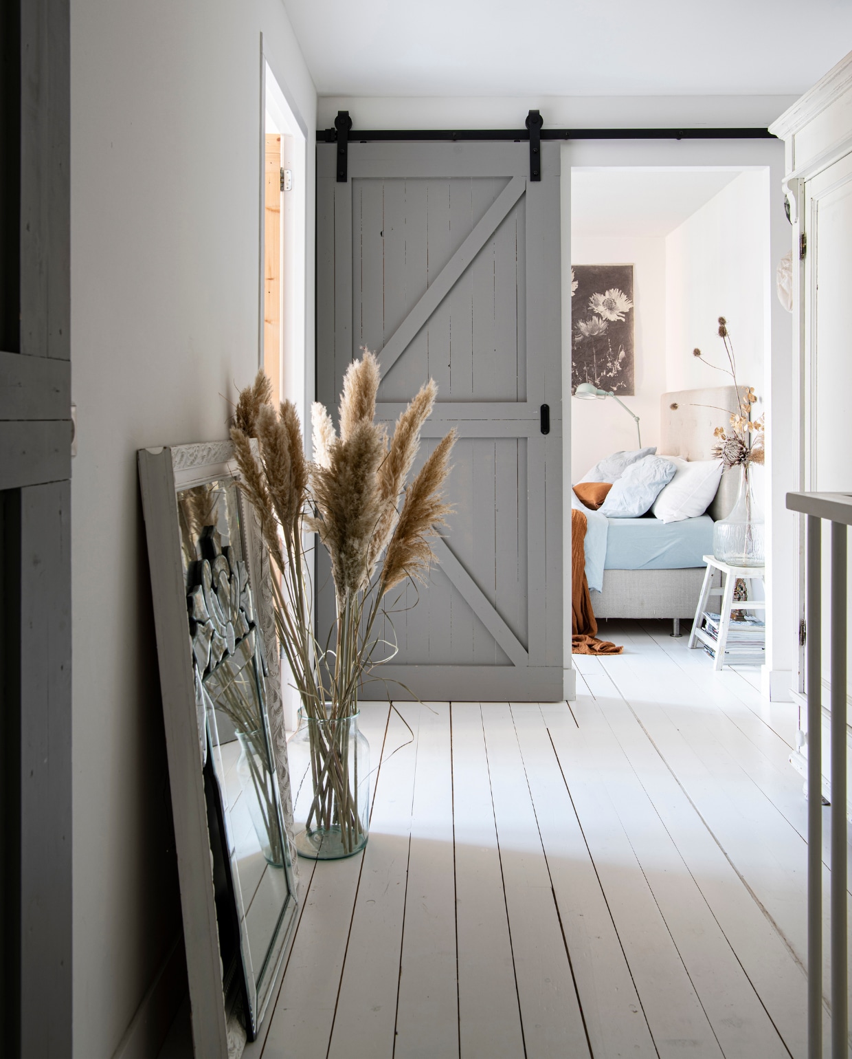 Houten vloer Pont Meyer Zaandam. Botanische print aan de muur Mo-ca. Bed Ikea. Lamp Made. Blauw beddengoed Dutch Home Fabrics. Plaid H&amp;M Home. Kruk tweedehands. Vaas op kruk Zuiver. Spiegel in de hal tweedehands. Vaas Loods 5. Schuifdeuren gemaakt door aannemer. vtwonen 09-2020 | productie Insidehomepage | fotografie Louis Lemaire | styling Marit Saladini