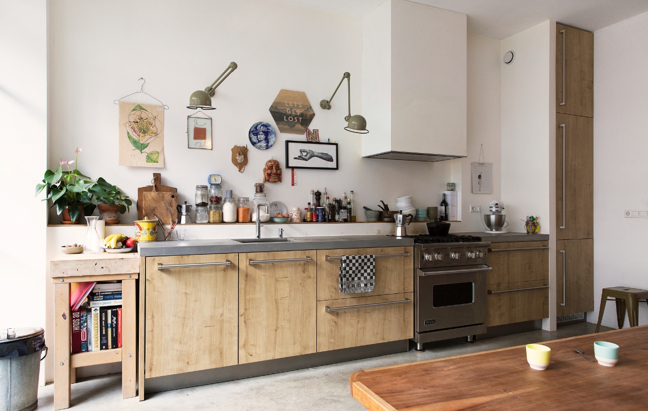 De keuken van Siematic, met een gasfornuis van Viking, geeft door de houten look een warme uitstraling bij de wat killere betonvloer. Ook op het aanrecht mag alles worden gezien. Muurlampen van Jieldé, prullenbak van de rommelmarkt. Kruk van Tolix. vtwonen binnenkijken special 121-2017 | styling Emmy van Dantzig | fotografie Jansje Klazinga