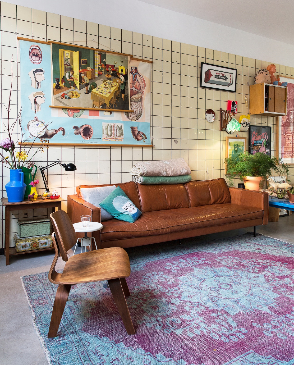 Deze kant van het huis is de straatkant. Waar nu een mooi kleed van Loods 5 ligt, zat eerst een groot gat in de vloer, zodat de garagemedewerkers onder de auto’s konden kijken. Leren bank van Loods 5, blauw kussentje en kussen met gezicht van Spira. Houten tafel naast de bank en blikken eronder van de rommelmarkt. Vazen van Een bloemetje op tafel. Het houten stoeltje stond om de hoek van de straat op de stoep, klaar voor het grofvuil. Witte kruk van Dulton Company, zwarte lamp Ikea. Groene dekens van een rommelmarkt, de andere van Ferm Living. Grote schoolposters van Spullen voor je huis. vtwonen binnenkijken special 121-2017 | styling Emmy van Dantzig | fotografie Jansje Klazinga