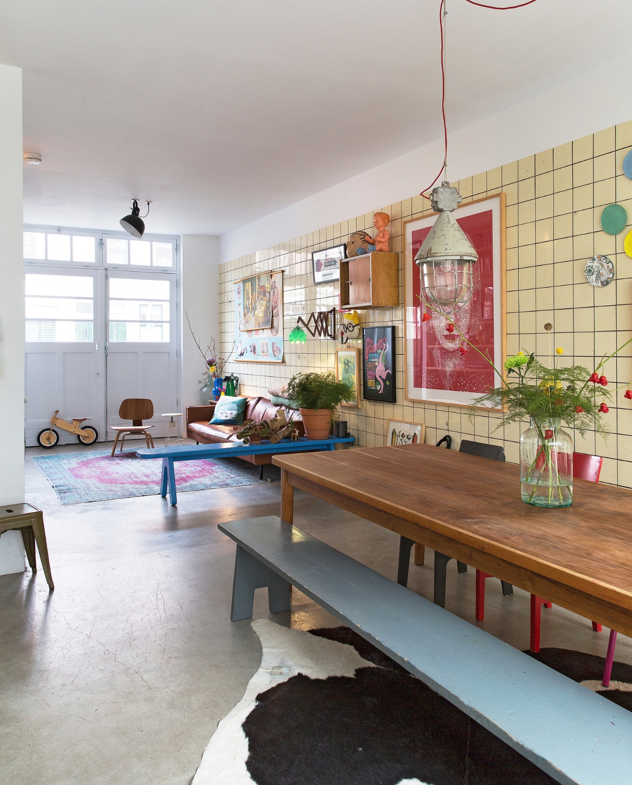 Eettafel gevonden in een oude loods die niet meer bestaat, grijze bank zelf gemaakt. Stoelen van Piet Hein Eek, Eames (Vitra) en gevonden bij het grof vuil. Hanglamp van een boorplatform gekocht bij Neef Louis. Vazen ‘van de mooiste bloemenwinkel in Rotterdam’: Een bloemetje op tafel. Bank en kleed Loods 5. Blauwe bank gemaakt door Frank de Bruijn van Supergoed. Groene lamp van Snowpuppe. Kastje en veel kaarten aan de muur van Spullen voor in je huis. Rood kunstwerk van Inez Odijk, schilderij met aap van Freya Wisman, werk in zwarte lijst van Piet Parra, bord met gezicht van Donna Wilson. Witte kruk achterin van Dulton Company, kruk op de voorgrond van Tolix, koeienhuid van Ikea. vtwonen binnenkijken special 121-2017 | styling Emmy van Dantzig | fotografie Jansje Klazinga