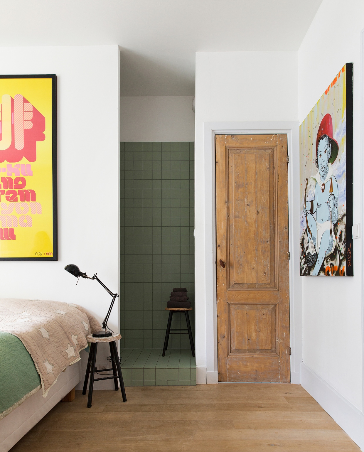 In eerste instantie wilden Job en Jol een andere kleur tegel voor de badkamer in hun slaapkamer, maar die moesten besteld worden en dat zou weer te lang duren. Deze pistachekleur, ‘Niemand wilde ze’, konden ze meteen meenemen en geven een prachtig samenspel met de houten vloer. De houten deur vonden ze in hun schuur. Zeefdruk boven het bed van The Designers Republic. Het schilderij van de baby is gemaakt door Rah Crawford. Plaid van Ferm Living, lamp van Ikea, krukken van een rommelmarkt. vtwonen binnenkijken special 121-2017 | styling Emmy van Dantzig | fotografie Jansje Klazinga