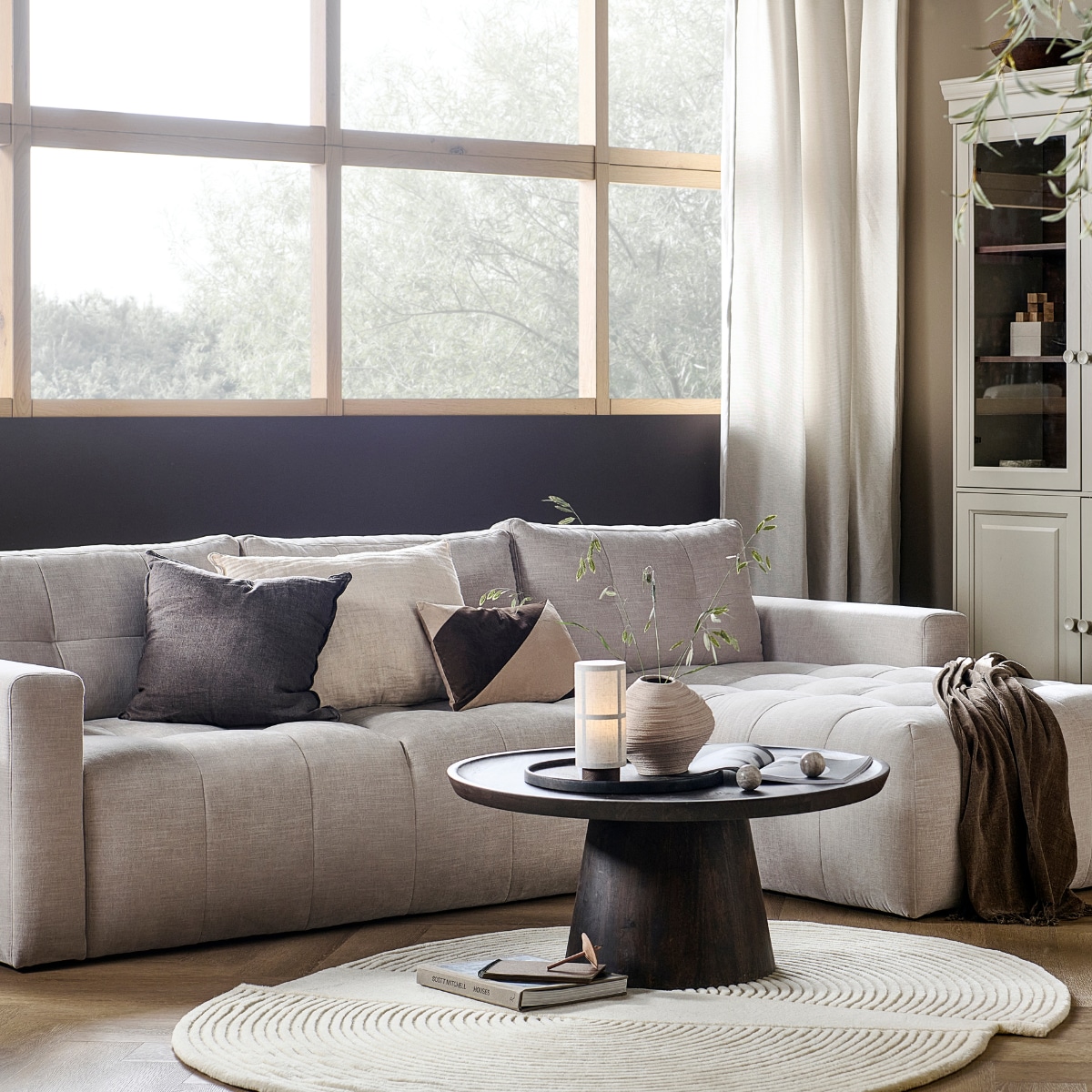 vtwonen collectie (Bank Bar met chaise longue rechts in zand, 280x170x87 cm (bxdxh) € 1749,-, ook met chaise longue aan de linkerkant en in antraciet, groen, roze en warmgrijs. Grenenhouten vitrinekast Chow 2-deurs in Dakargrau, 54x40x215 cm (bxdxh) € 499,-, ook verkrijgbaar als 4-deurs vitrinekast. Walnotenfineer salontafel Coffee a Gogo, 90x40 cm (Øxh) € 499,-. Mangohouten bijzettafel Beach Small in Clay, 64x51x53 cm (lxbxh) € 319,-, ook in 80x80x41 cm (lxbxh)). M.m.v. vtwonen.nl/shop (vloerkleed van Bolia, tafellamp van Menu, gestreept kussen van Moos), hm.com (beige aardewerken vaas, bruine plaid), karwei.nl (muurverf Mirre en Warm Brown). Overig privébezit. vtwonen 05-2023 | productie Tanja Saarberg | styling Sanne Ketelaar | fotografie Sjoerd Eickmans