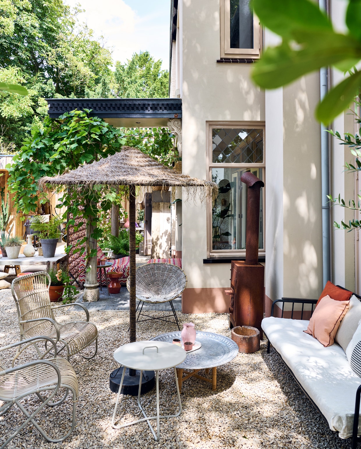 Buitenkachel Weltevree. Tuinbank en witte bijzettafel Kwantum. Tuinstoelen Sissy-Boy, kuipstoel Kave Home, parasol Household Hardware, lage bijzettafel Ottomania, kan souvenir Italië, schaal met kommetjes souvenir Lissabon, kussens H&M Home, betonnen pot Intratuin. Overige zie andere fotobijschriften.