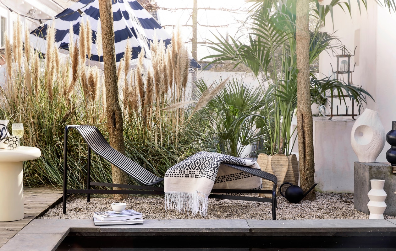 Antraciet daybed Palissade van Hay, gepoedercoat staal, 164,5x65,5x70 cm (lxbxh) € 999,-, zwart-witte waxinelichthouder € 4,95 (loods5.nl). Parasol Stripesol, 350 cm (Ø) € 479,- (fatboy.com). Wollen plaid € 172,50, polyester bijzettafel, 50x50 cm (Øxh) € 359,-, zwarte tadelakt vaas Bubbles € 119,-(householdhardware.nl). Gerecycled wijnglas € 19,50 (serax.com). Zwart-witte kan van Bachmara € 29,90 (ateliersem.nl). Plantenpot met ribbels € 195,-, vaas met gat € 91,95 (ptmd.nl). Witte kom Kyoto € 6,-, witte vaas met zigzag-reliëf € 38,- (hkliving.com). Vintage flessenrek € 89,- (cininwonen.nl). Gieter privébezit. vtwonen 06-2023 | styling Kim Timmerman | fotografie Peggy Janssen