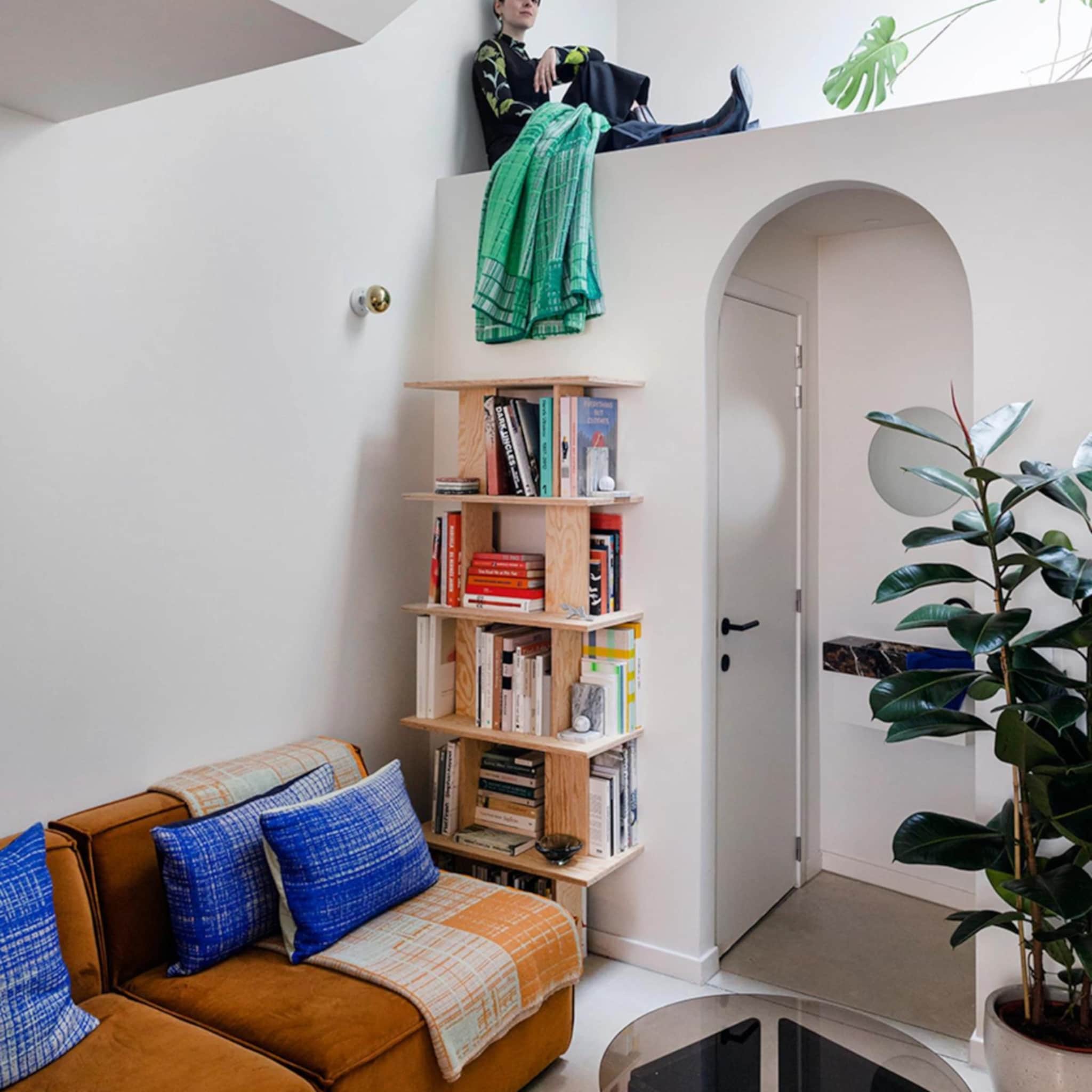 Zitgedeelte met oranje bank en blauwe kussens en een hoge muur met ruimte voor een zitplek daarboven