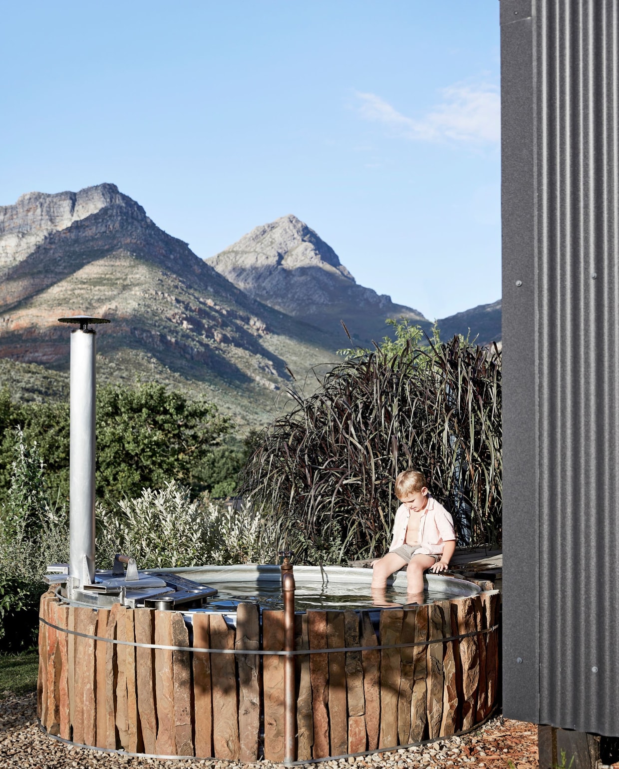Silas aan het pootjebaden in het speciaal voor deze plek gemaakte, verwarmde en met ruw hout beklede buitenbad, ontworpen door Spaas. vtwonen binnenkijken special 171-2021 | styling Sven Alberding | fotografie Warren Heath/Bureaux