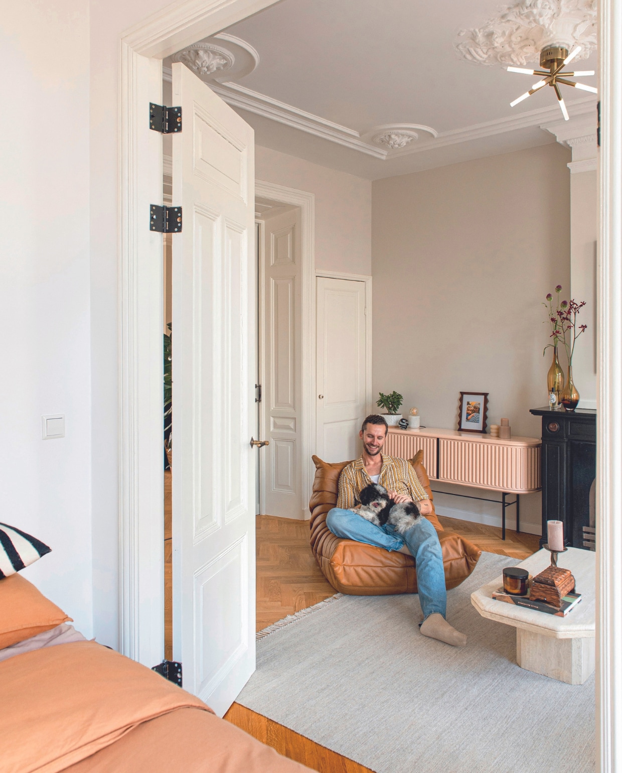 Koffietafel Marktplaats, onderzetters uit New York. Kistje en kandelaar kringloopwinkel. Vloerkleed CarpetVista, vintage fauteuil Togo van Ligne Roset, dressoir Pastoe, presse-papier uit Engeland, vaas op dressoir bouwmarkt. Fotolijst en kandelaar H&amp;M Home. Glazen vazen vintage, plafonnière Made. Openslaande deuren Leen van Velzen. Overig onbekend. vtwonen 05-2024 | productie De Binnenkijkers | styling Jeske Weel | fotografie Caroline Coehorst