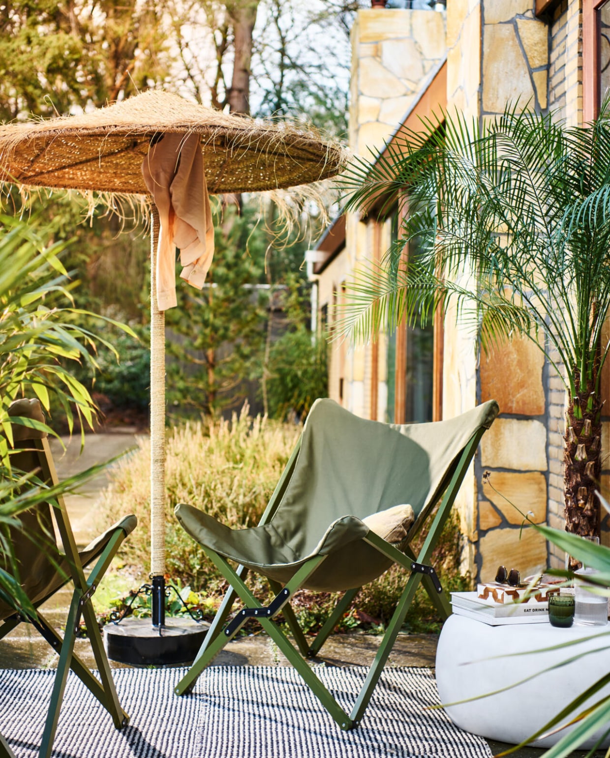 vtwonen collectie (opvouwbare buitenstoelen Lazy Afternoon in camouflage groen, 85x77x92 cm (bxdxh) € 169,-, fiberclay bijzettafel Pebble in betonlook wit, 65x49x31 cm (bxdxh) € 199,-, ook verkrijgbaar in 50x35 cm (Øxh) € 179,- en in antraciet). M.m.v. householdhardware.nl (parasol, parasolvoet), vtwonen.nl (kussen, waterglas). Overig privébezit. vtwonen 04-2023 | productie Tanja Saarberg | styling Marlies Does | fotografie Sjoerd Eickmans