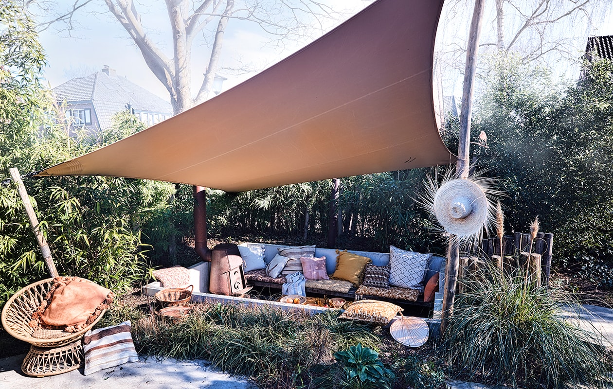 Tent schaduwdoek op maat gemaakt (tentworx.nl). Hoed, gestreept berber kussen 50×50 cm, ecru kelim kussen met pijl 50×50 cm, groot berber kussen met schuine ruit 80×80 cm, groot gestreept kussen 75×75 cm, roze kelim kussen 50×50 cm, decoratief waaier, bamboe salontafel van Tine K Home 70x150x45cm (bxlxh), manden in het gras, naturel linnen handdoek van Libeco (couleurlocale.eu). Gedessineerde matraskussens 60×100 cm, grote kussens met kwasten 65×65 cm, kussen met oranje batik dessin 50×50 cm, kussen met bordeauxrood en oranje dessin 50×50 cm, allemaal Madam Stoltz (deens.nl). Ronde rattan draaistoel Peacock van Arti 89x81x73 cm (lxdxh) (fonteyn.nl). vtwonen TUIN 02-2020 | styling Cleo Scheulderman | fotografie Jeroen van der Spek