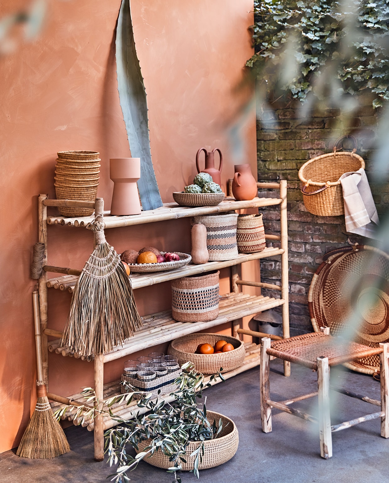 Muur geschilderd met buitenverf Kalei in Dry Terra van Pure &amp; Original, per 5 liter € 225,80 (deruamsterdam.nl). Bamboe rek van Tine K Home, 110x150x40 cm (hxlxb), olijfhouten kruk met oranje zitting, 45×45 cm, mand met hengsels, oranje sisal manden, Iraca palm schalen, mand Ghana aan de muur, platte palmblad schaal, hoge mand met ribbels Gogo (couleurlocale.eu). Terracotta vaas met oren, terracotta vaas met één oor, lichtoranje vaas (nordal.eu). Bezem, bezem met houten steel van Madam Stoltz (deens.nl). vtwonen tuin special 2 2020 | styling Cleo Scheulderman | fotografie Jeroen van der Spek