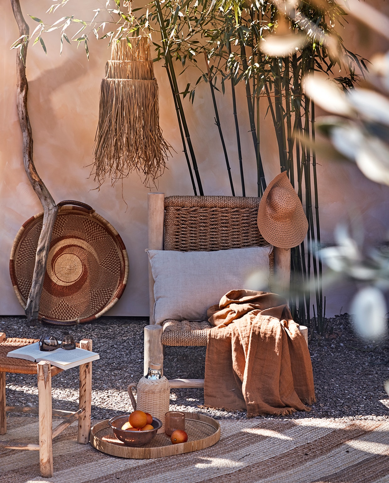 Muur geschilderd met buitenverf Kalei in Sahara Dust van Pure &amp; Original, per 5 liter (deruamsterdam.nl). Stoel Charlotte, amberkleurig linnen plaid, muurmand Ghana, olijfhouten kruk met oranje zitting, 45×45 cm (couleurlocale.eu). Vloerkleed van Madam Stoltz, 200×140 cm, rieten lampenkap (deens.nl). Rieten thermoskan, glas, dienblad (nordal.eu). Naturel linnen kussen van vtwonen, 50×70 cm (vtwonen.nl). Overig privébezit. vtwonen tuin special 2 2020 | styling Cleo Scheulderman | fotografie Jeroen van der Spek