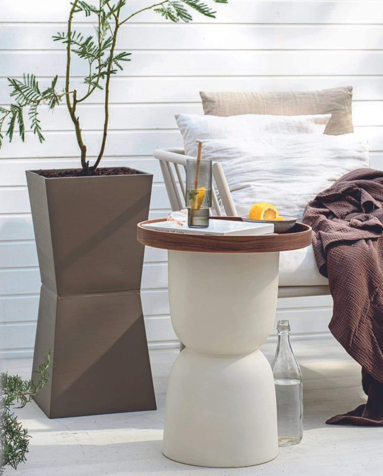 Mimosa boom € 59,95, rozemarijn € 24,95 (bloementuinaandezaan.nl). Aluminium bankelement Menton € 299,- (jotex.nl). Longdrinkglas Ripple van Ferm Living in Smoked Grey, set van 4 € 59,- (thefinestore.com). Parasol Pescara van Human Nature, 180 cm (Ø) € 44,99 (anwb.nl). Beige linnen kussenhoes € 14,99, mousseline sprei, 180x250 cm € 69,99, linnen gordijnen, set van 2 € 84,99 (hm.com). Witte linnen kussenhoes Milk € 19,-(puurlifestyle.com). Houtfineer dienblad Ombonad, 42 cm (Ø) € 34,99 (ikea.nl). Overig privébezit. vtwonen 06-2024 | styling Myla Griese | fotografie Louis Lemaire