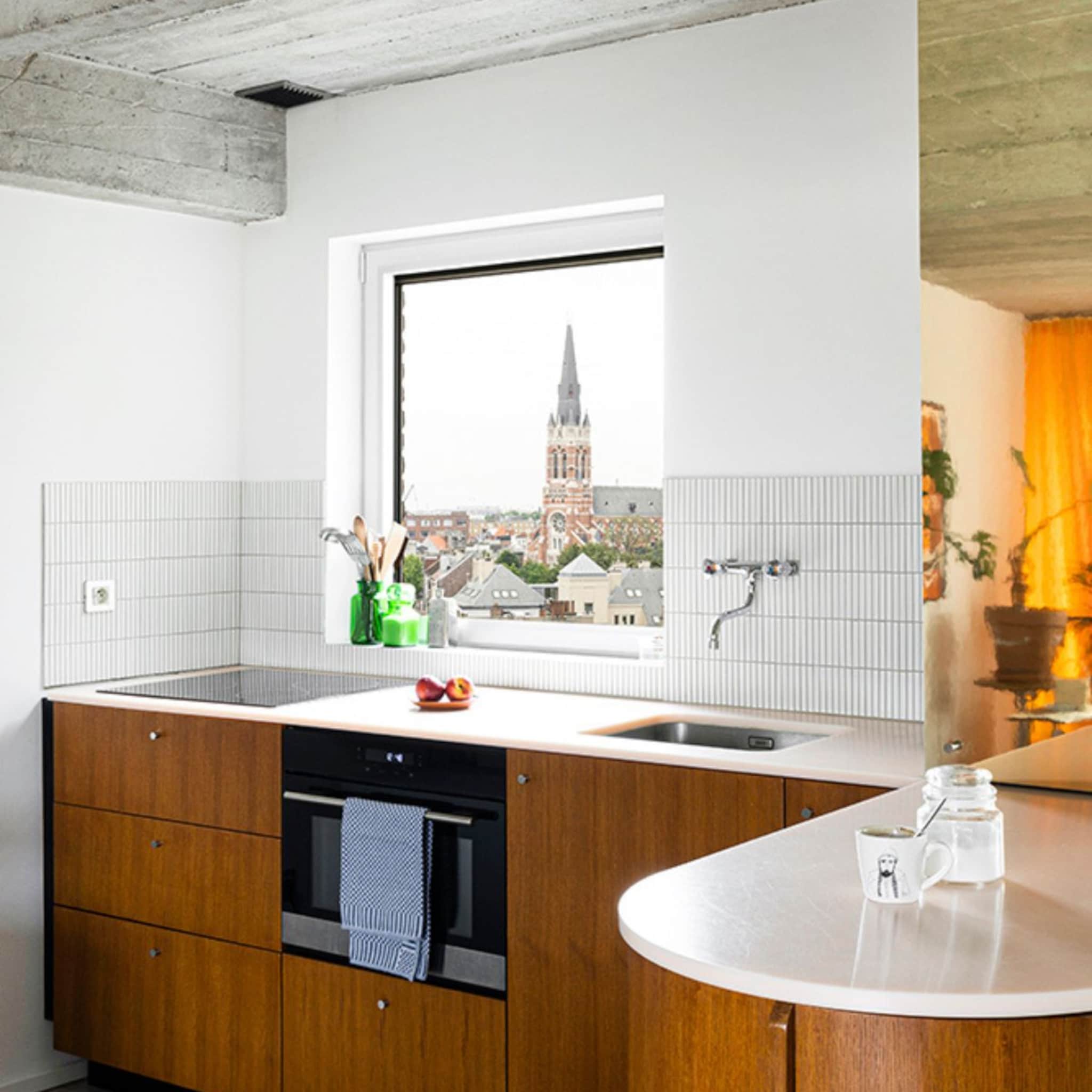 Keuken met houten kastjes en wit aanrechtblad met uitzicht op een kerktoren in Antwerpen