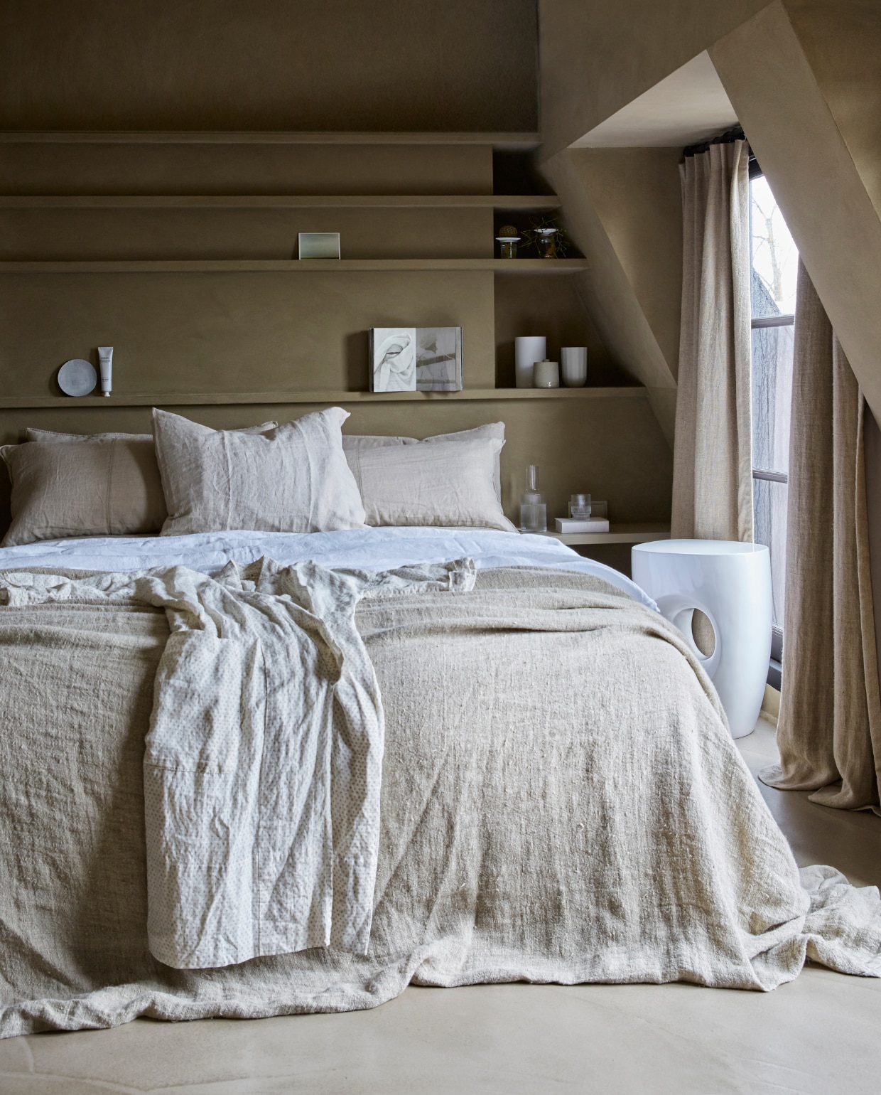 Muurverf Buffalo, prijs op aanvraag (Tribe). Vloer prijs op aanvraag (Pureconcept). Witte kruk, 35x40 cm (Øxh) € 251,- (Pols Potten). Bedsprei Natural, 270x270 cm € 229,- (HK Living). Linnen laken kleur Pure White, 160x255 cm € 119,-, voorste kussen kleur Flax, 60x70 cm € 30,- (By Mölle). Gordijnen kleur Stonewashed, prijs op aanvraag (Chivasso). Waterkan Ripple van Ferm Living € 34,-, glas Ripple van Ferm Living, set van 4 € 40,-, voetencrème van Meraki € 11,95, taupe vaas van D&amp;M Depot € 9,95, paper vaas van Hay € 69,-, witte vaas van Menu € 54,95 (vtwonen.nl). Bord van Frédérick Gautier € 14,95 (Serax). Kaart vanaf € 0,90 (artlimited.net). Boek Out of Fashion (Birgitta de Vos). Plantjes (Sprout). Kimono (Sukha Amsterdam). Op maat gemaakte kast en kussens privébezit. vtwonen 08-2018 | Styling Marianne Luning | Fotografie Tjitske van Leeuwen