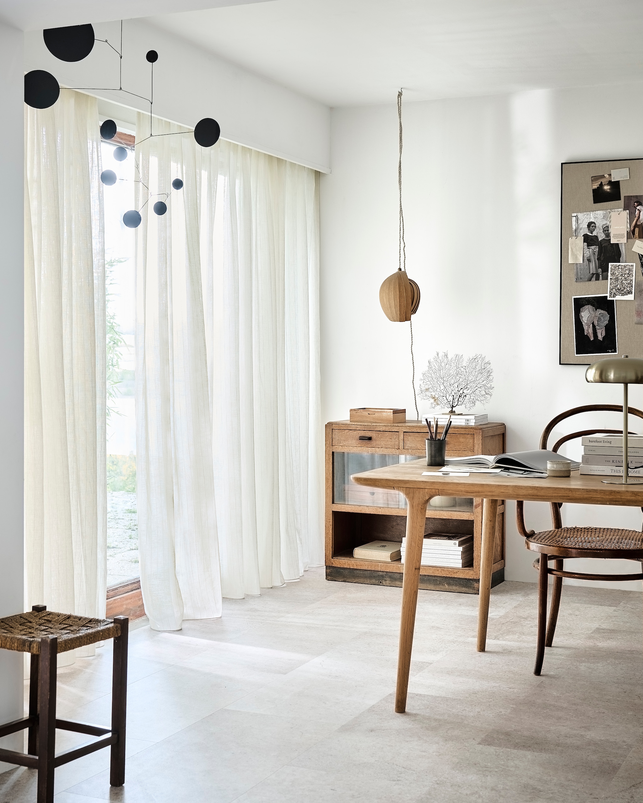 Inbetween transparant gordijn op maat in stof Wide Stripes, kleur Ecru White Stripe (2316), per meter vanaf € 27,99.M.m.v. kringloop (kruk, kast), zarahome.com (prikbord, tafellamp, pennenbak), demuseumwinkel.com (zeewaaier), moduleo.com (vloer), lpln.de (mobile).   vtwonen 08-2024 | styling Kim van Rossenberg | fotografie Sjoerd Eickmans