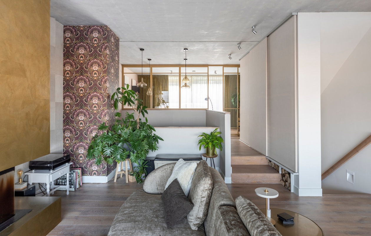 Flexa Creations muurverf Wit Sesam (flexa.nl). Beige leren wandtegels, prijs op aanvraag (enzopellini.nl). Haard bewerkt met een speciale verftechniek Lisboa Bronze, per m2 € 60,- (instagram.com/wecreatewalls). Rolgordijnen in de weving flat sticks vanaf € 298,- (zonnelux.nl). Bank van Passe Partout, per element vanaf € 1485,-, vloerkleed van Layered € 1490,- (eijerkamp.nl). Tafellamp op de gouden tafel van Umage € 199,-, vierkant bruin kussen van Essenza € 39,95, wit kussen van vtwonen € 58,99, plaid van Woood € 79,95 (vtwonen.nl). Vloerlamp van vtwonen € 179,95, zwarte onderzetters € 27,50, kandelaar vanaf € 12,50 (pand-40.nl). Kom van Light &amp; Living € 28,95 (dutchhomelabel.nl). Overig privébezit. vtwonen weer verliefd op je huis seizoen 16 aflevering 8 | styling Eva van de Ven | fotografie Margriet Hoekstra