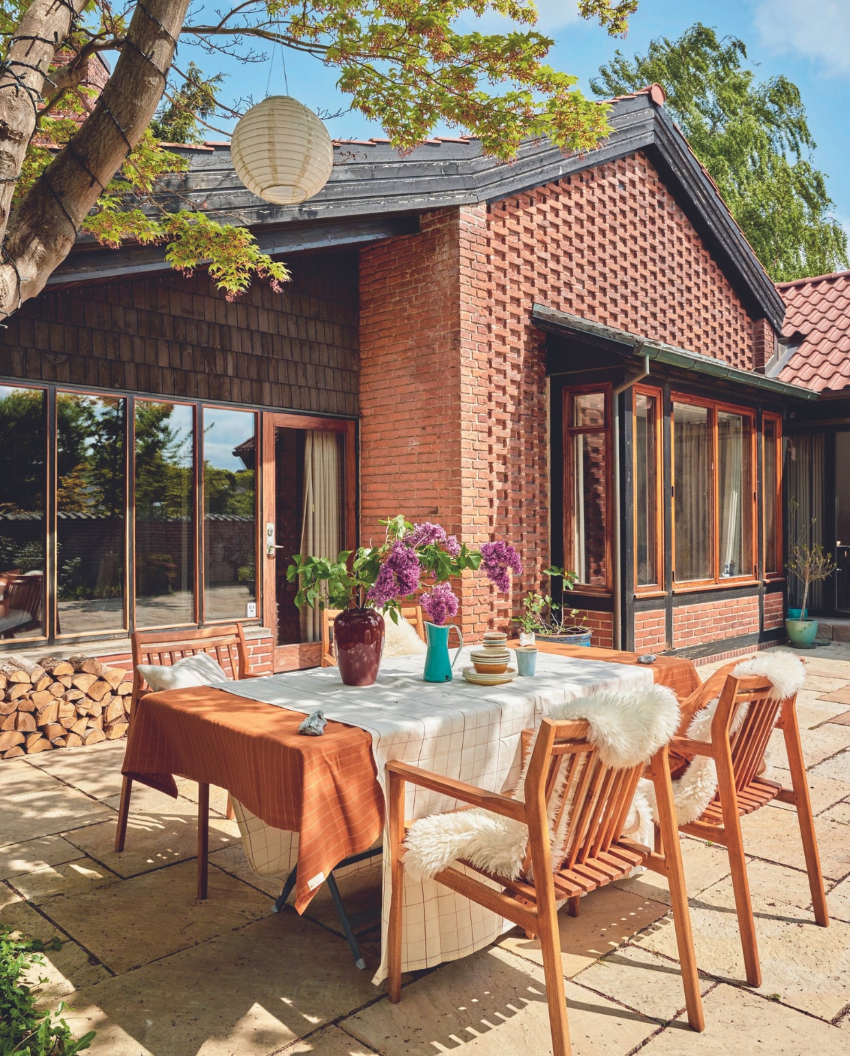 Terras aangelegd door de vorige bewoners, tuintafel Fermob, stoelen Fdb Møbler, vachten Ikea. Tafelkleden en servies Fabelab. Vazen vintage. vtwonen 06-2024 | fotografie Christina Kayser Onsgaard | styling Rikke Graff Juel