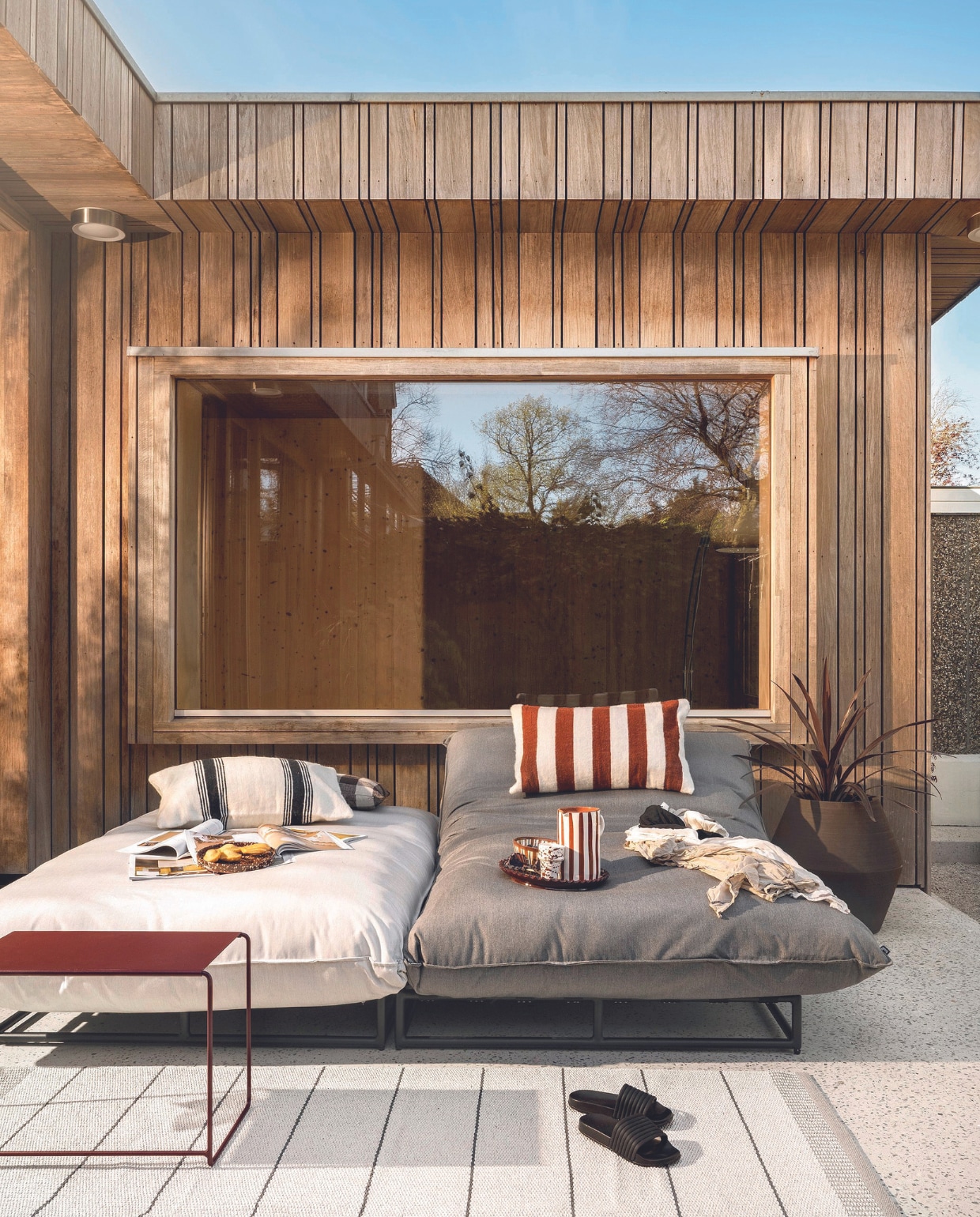 Loungebedden Emma, aluminium en all weather textiel, 196x130x40 cm (lxbxh) per stuk € 1199,- (hartman.nl). Stalen bijzettafel Oulala van Fermob, set van 3 € 299,-, buitenkleed Pappelina, 140x200 cm € 395,- (extravert.nl). Stenen bloempot Construct van Serax € 550,-, geruit linnen kussen Woven van HKliving € 49,95 (vtwonen.nl/shop). Gestreepte wollen kussens € 95,-, keramieken karaf, bord en kom vanaf € 16,50, keramieken mok Beldi € 12,95 (householdhardware.nl). Slippers (hema.nl). Overig privébezit. vtwonen 07-2024 | styling Marianne Luning en Kelly van Gendt | fotografie Stan Koolen