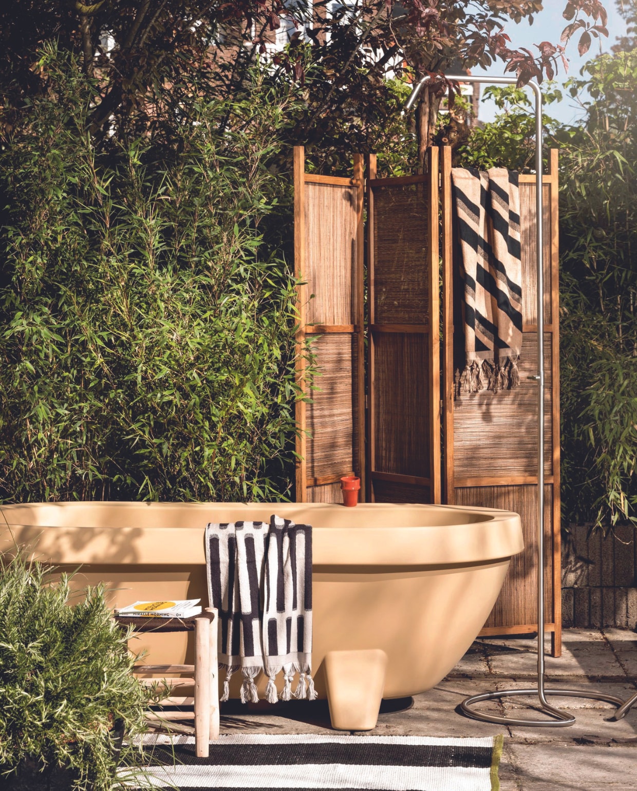 Kunststof bad in Sand Dune, 194x94x66 cm (lxbxh) € 1450,- (gardentub.com). Rvs buitendouche Serpentine € 295,- (weltevree.nl). Buitenkleed Saliya Noir van Designers Guild, gerecycled pet, 180x250 cm (wva.nl). Houten kruk € 69,50, keramieken mok Beldi € 8,50 (householdhardware.nl). Kamerscherm Coco, gerecycled teakhout en handgeweven palmblad, 145x195 cm (bxh) € 409,- (hetkabinet.nl). Katoenen handdoeken 1984 en 1991 van HKliving, per stuk € 49,95 (vtwonen.nl/shop). Overig privébezit. vtwonen 07-2024 | styling Marianne Luning en Kelly van Gendt | fotografie Stan Koolen