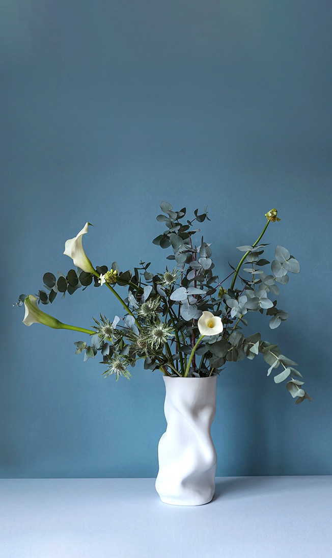 Het advies: De organische vorm van vaas Collapse van Menu matcht goed met het weelderige groen: eucalyptus en distels aangevuld met enkele calla lelies. De scherpe distels vormen een interessant contrast met de zachte vormen van de vaas, terwijl de lelies net die gebogen lijnen herhalen. Distel, eucalyptus en calle lelies zijn het hele jaar door beschikbaar. Het is een handige combinatie waar je altijd naar kunt teruggrijpen. Fotografie Kaatje Verschoren