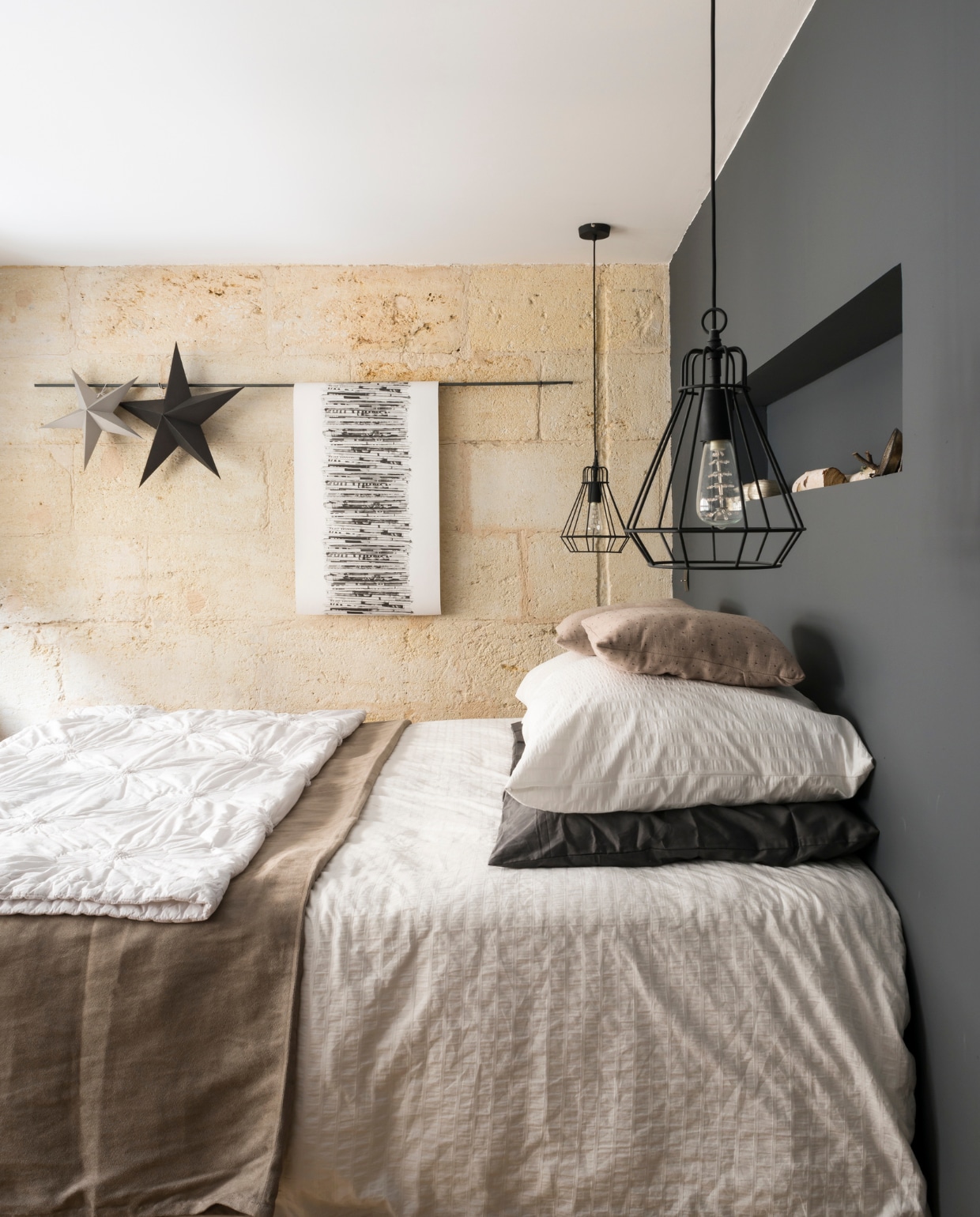 Eyecatcher in de ouderlijke slaapkamer is de originele stenen muur. De antracietkleurige wand biedt een eigentijds tegenwicht. Het bedlinnen is van Ikea, www.madurahome.com en Côté Table. De lampen zijn van Castorama, een Franse bouwmarkt. De print is een stuk behang. Bron: vtwonen 03-2015 | fotografie Julien Fernandez, amandinejules.com | tekst Amandine Berthon | tekstbewerking Monique van der Pauw