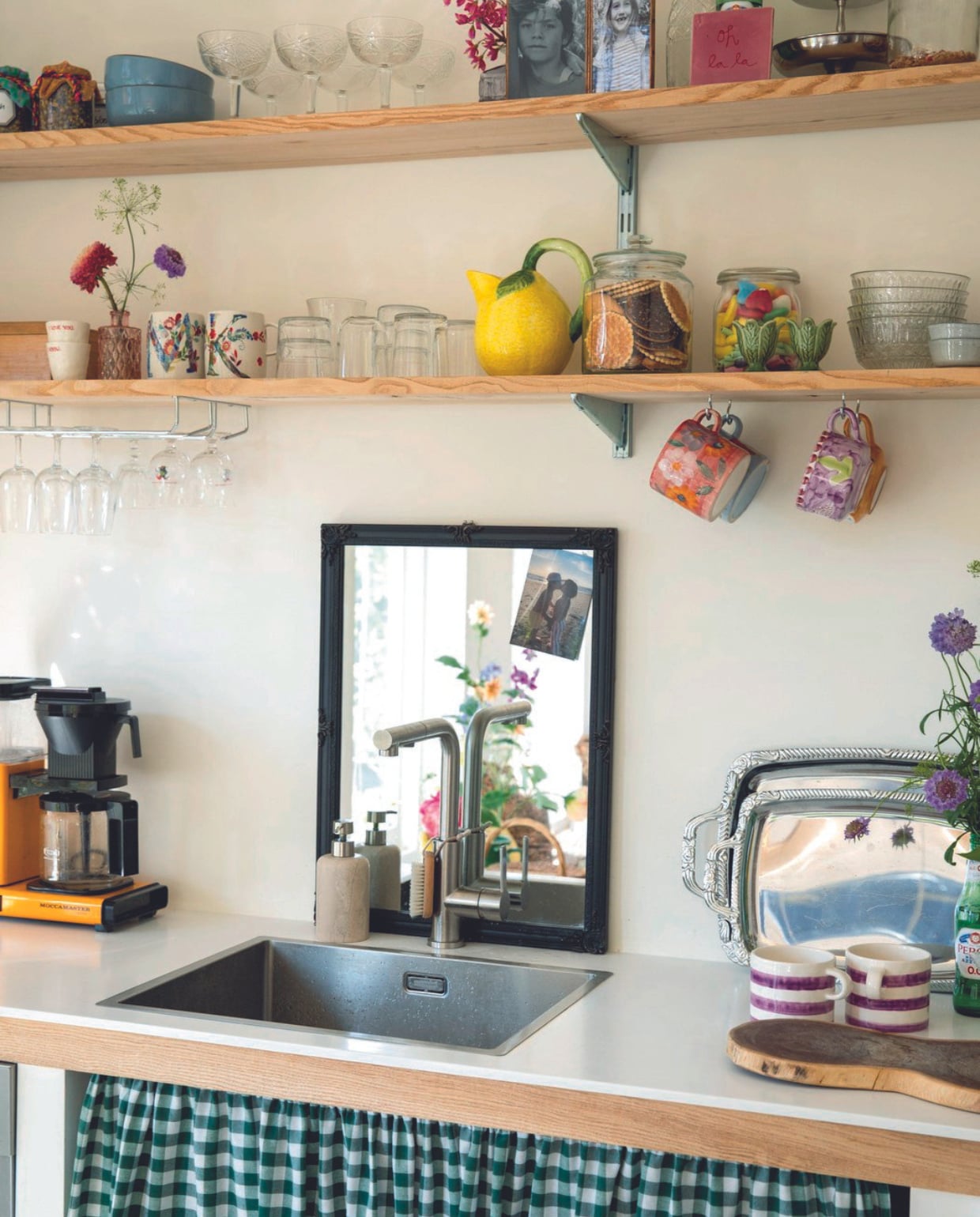 Keuken zelfgemaakt, geblokte gordijnstof Albert Cuyp. Mokken met paarse strepen, dienbladen, spiegel, hangende mokken Anna + Nina. Koffiezetapparaat Moccamaster, wandplanken Amsterdamsche Fijnhout, mokken bloemen Anthropologie, glazen Loods 5, citroenvormige kan Les Ottomans, tegel Lemonwise, etagère vintage, servies Sissy-Boy.
