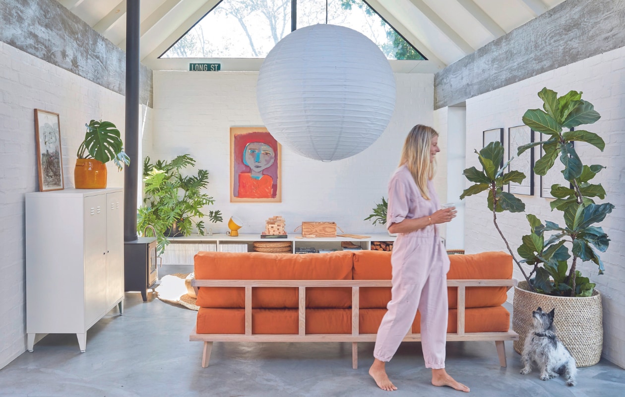 Maatwerk bank Kipekee Studio, stof in Tobacco van House of Fabrics (Kaapstad). Dressoir zelfgemaakt door Casey, ontwerp Beatty Vermeiren. Schilderij Jan Vermeiren, tafellamp Ikea PS collectie. Kachel Morsø, kast Mother City Hardware, gele plantenpot Pezula, muurverf Dulux. Vergelijkbaar: rijstpapieren hanglamp Hay, mand Urban Nature Culture. Planten onder andere Monstera en Ficus lyrata.