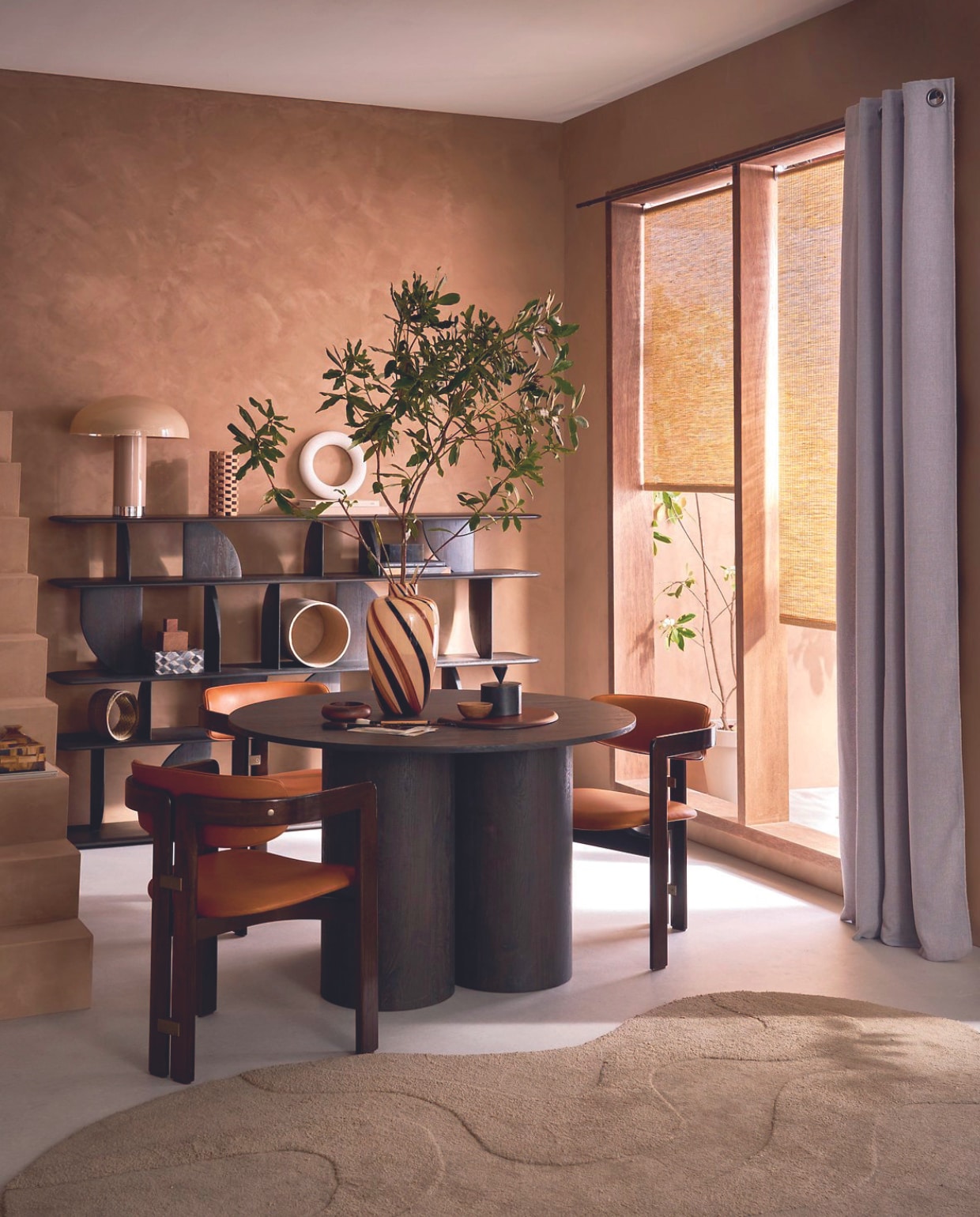 Lichtdoorlatende rolgordijnen Aftersun, 90x190 cm (bxh), per stuk € 78,99. Lichtdoorlatend gordijn Denim in antraciet met ring, 140x270 cm € 62,99.M.m.v. lauthentique.nl (kalkverf in Mokka), basiclabel.nl (eettafel Oona van Woood, vloerkleed Alya van Woood), melchiorinterieur.nl (vakkenkast van Ethnicraft), @iconic_objects (eetkamerstoelen Pamplona van Savini), vtwonen.nl/shop (snijplank van Ferm Living, tafellamp en vaas van HKliving). Overig privébezit. vtwonen 07-2024 | styling Cleo Scheulderman | fotografie Jeroen van der Spek