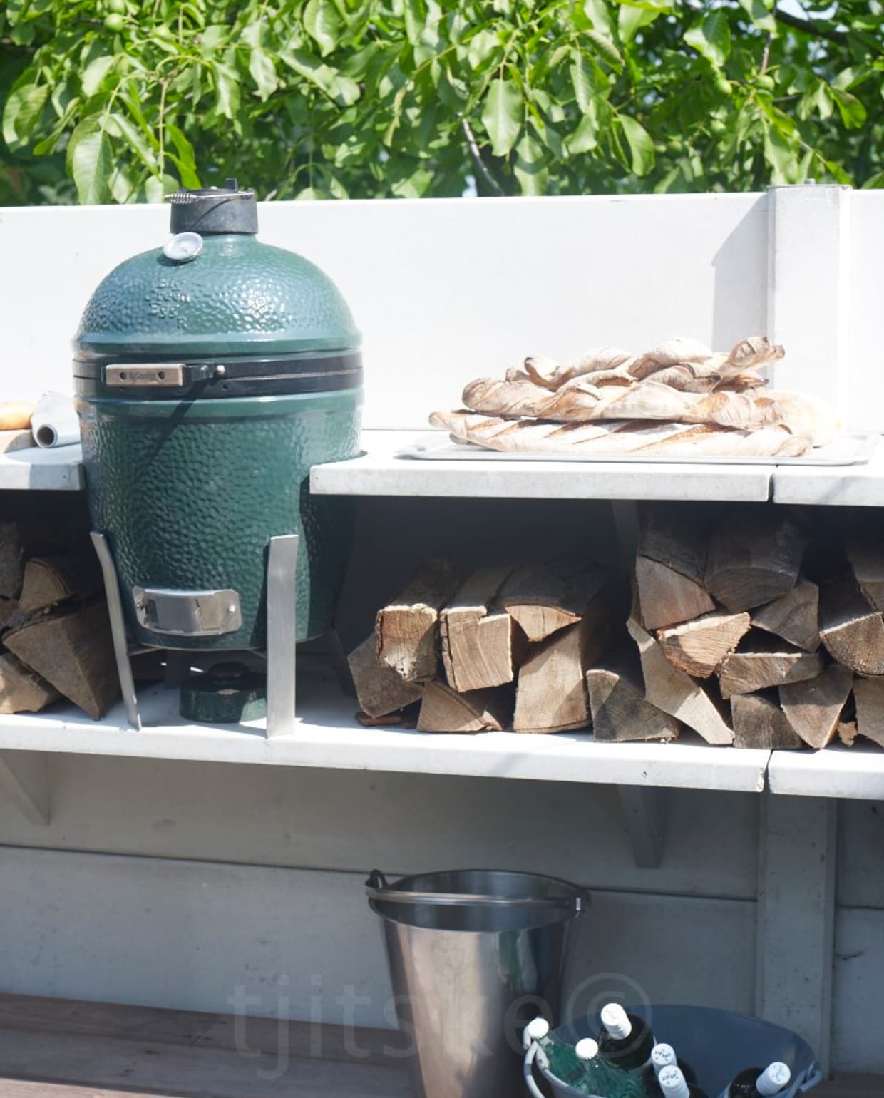 Buitenkeuken Wwoo, ontwerp Piet-Jan van den Kommer, opgebouwd uit verschillende betonnen delen 150x140 (bxh) verkrijgbaar in grijs en antraciet vanaf € 987,- per deel. Barbecue Big green Egg € 598,95, rvs wasbak met kraan en aansluiting voor een tuinslang van Gardena € 489,25, rvs vuurbak met hittebestendige achterwand € 464,50, houten kistje € 149,25, olijfhouten snijplank 30x20 cm € 41,25, grilltang € 21,50, houten buitenvloer, grote tafel en banken prijs op aanvraag (www.wwoo.nl). Bruin servies Dinera 18-delig € 24,95, glazen flessen met dop € 1,99 per stuk (Ikea). Diverse metalen emmers en bakken vanaf € 9,50, kleinere metalen bakjes vanaf € 5,95, oude linnen loper € 14,95 (Combitex). vtwonen 05-2021 | fotografie Tjitske van Leeuwen | styling Fietje Bruijn | productie Corrien Flohil