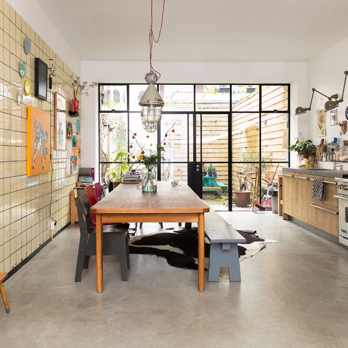 Eettafel gevonden in een oude loods, grijze bank zelf gemaakt. Stoelen van Piet Hein Eek, van Eames gevonden bij het grofvuil. Hanglamp van Neef Louis. Vazen van Een Bloemetje op Tafel. Bank en kleed Loods 5. Blauwe bank gemaakt door Frank de Bruijn van Supergoed. Groene lamp van Snowpuppe. Kastje en veel kaarten aan de muur van Spullen voor in je huis. Rood kunstwerk van Inez Odijk, schilderij met aap van Freya Wisman, werk in zwarte lijst van Piet Parra, bord met gezicht van Donna Wilson. Witte kruk achterin van Dulton Company, kruk op de voorgrond van Tolix, koeienhuid van Ikea. vtwonen special binnenkijken 121-2017 | styling Emmy van Dantzig | fotografie Jansje Klazinga
