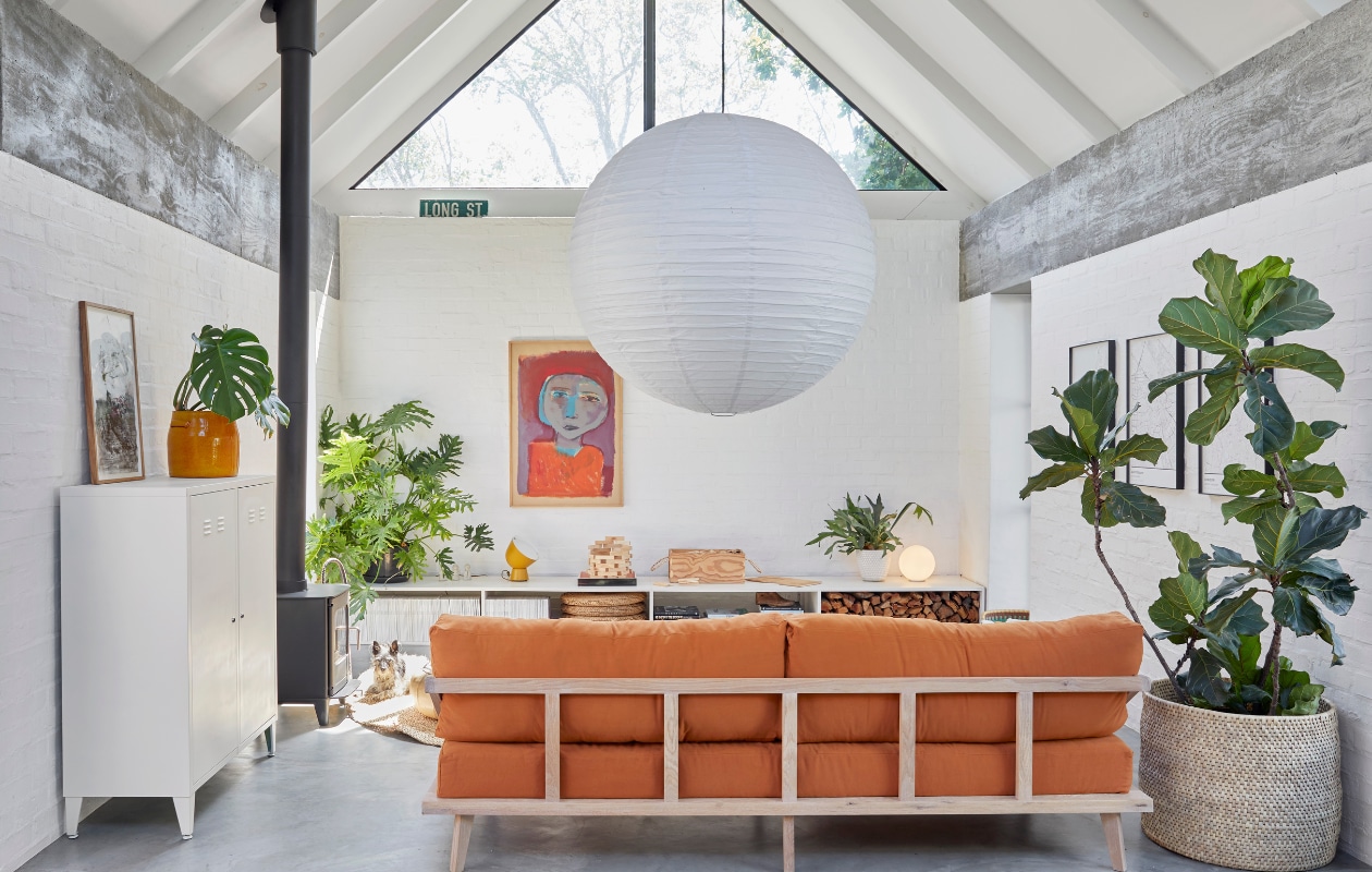 Maatwerk bank Kipekee Studio, stof in Tobacco van House of Fabrics (Kaapstad). Dressoir zelfgemaakt door Casey, ontwerp Beatty Vermeiren. Schilderij Jan Vermeiren, tafellamp Ikea PS collectie. Kachel Morsø, kast Mother City Hardware, gele plantenpot Pezula, muurverf Dulux. Vergelijkbaar: rijstpapieren hanglamp Hay, mand Urban Nature Culture. Planten onder andere Monstera en Ficus lyrata. vtwonen 07-2024 | productie Frank Features / Living Inside | fotografie Greg Cox