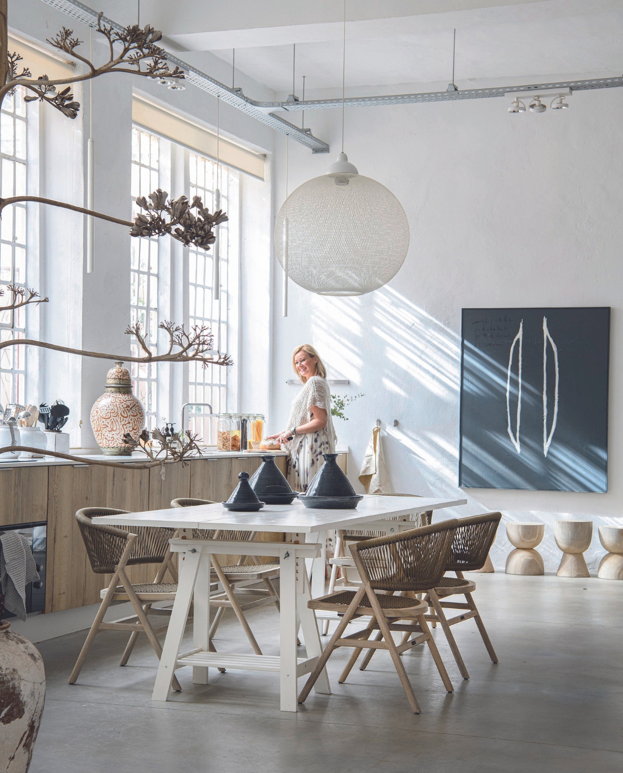 Tafel, eetkamerstoelen en krukken Max &amp; Luuk. Tajines en zwart-witte pot op voorgrond lokaal gekocht, keuken maatwerk, witte hanglamp Moooi, grote pot aanrecht vintage, vloer beton, schilderij Eric de Bruijn. vtwonen 07-2024 | productie Inside Homepage | styling Anja Bas Backer | fotografie Louis Lemaire | tekst Caroline Westdijk