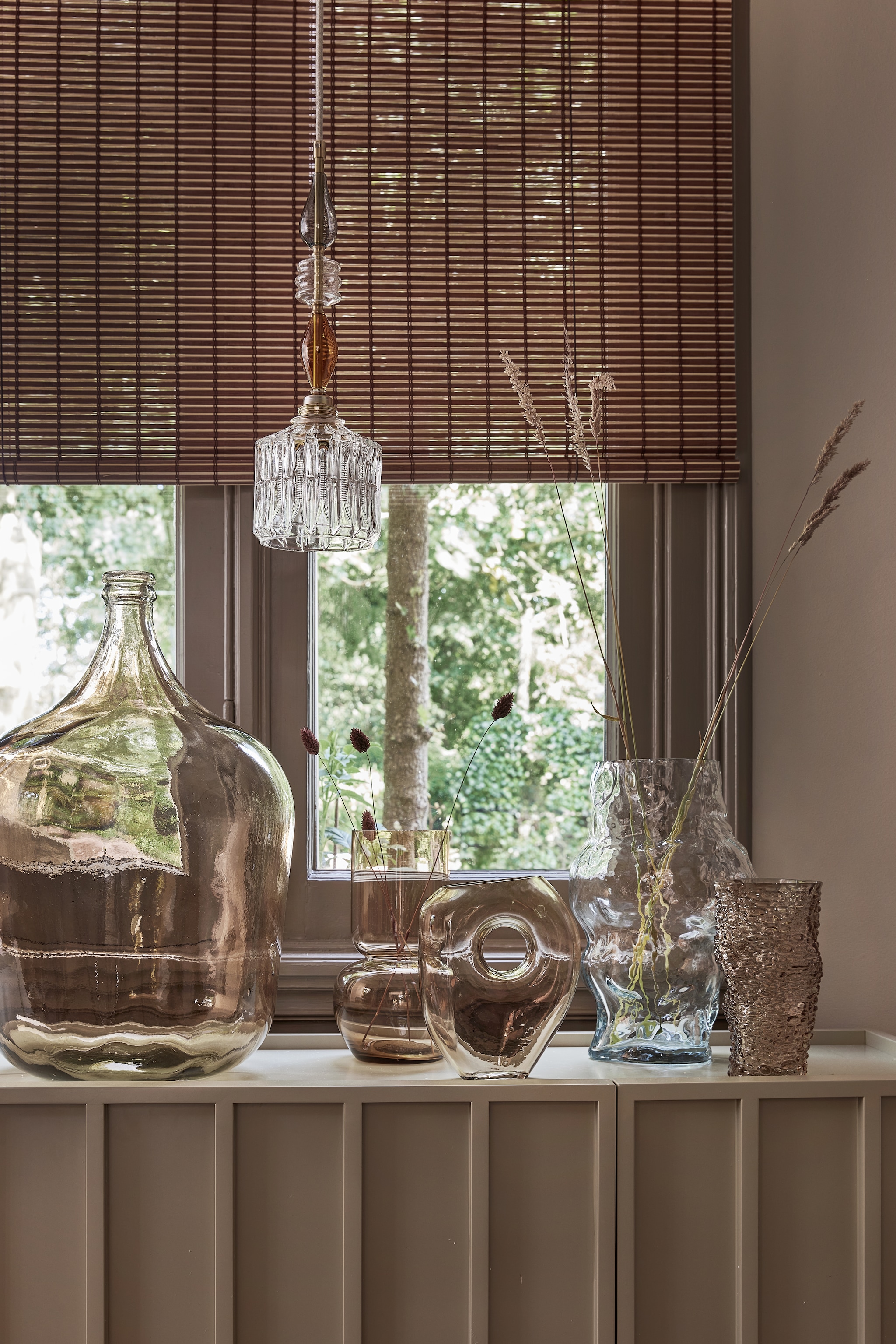 Glazen hanglamp vanaf € 250,- (memooi.nl). Glazen vazen van links naar rechts: bolvaas XL € 99,- en Nude € 32,50 (mrsbloom.nl), met gat € 29,95 (by-boo.com), Cloud € 59,95 (hkliving.nl), Grove € 12,50 (kwantum.nl). Bamboe rolgordijn € 35,95 (xenos.nl). vtwonen 10-2024 | styling Kim Timmerman | fotografie Peggy Janssen