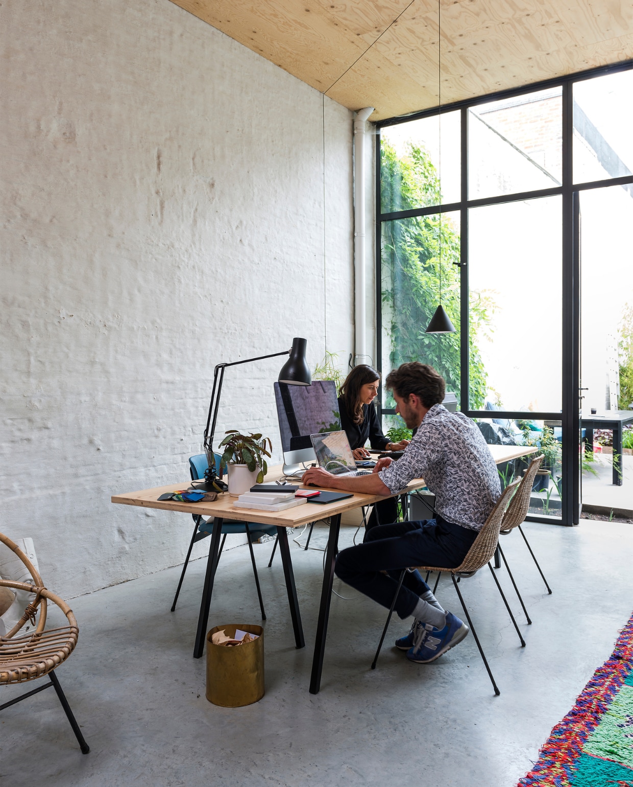 Leen en Tim werken in hun kantoor achteraan de tuin. Hier vonden vroeger elke zaterdag misvieringen plaats. De muren zijn nu wit en er ligt een betonvloer. De bureautafel is een eigen ontwerp, de bureaulamp is een Anglepoise type 75, de vintage rieten stoel van Sliedrecht, hanglamp String is een ontwerp van Anastassiades voor Flos en de koperen prullenmand kochten Leen en Tim in een designwinkeltje in Rotterdam vtwonen 10-2017 | Fotografie Stan Koolen