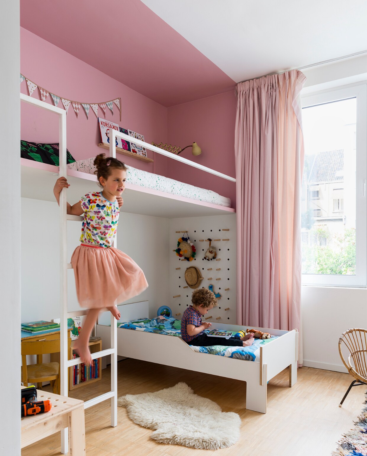 Warre en Marthe delen een kamer, maar hebben toch elk hun eigen ruimte. Tim maakte voor Marthe een eigen niveau dat in het roze werd geschilderd. In de schuine wand hebben de kinderen elk een open en gesloten kastje voor persoonlijke spulletjes. Ook het bed van Warre is zelfgemaakt, zonder vijzen. Omdat dit een jongens- en meisjeskamer tegelijk is, kozen Leen en Tim voor gordijnen in verschillende kleuren. vtwonen 10-2017 |  Fotografie Stan Koolen