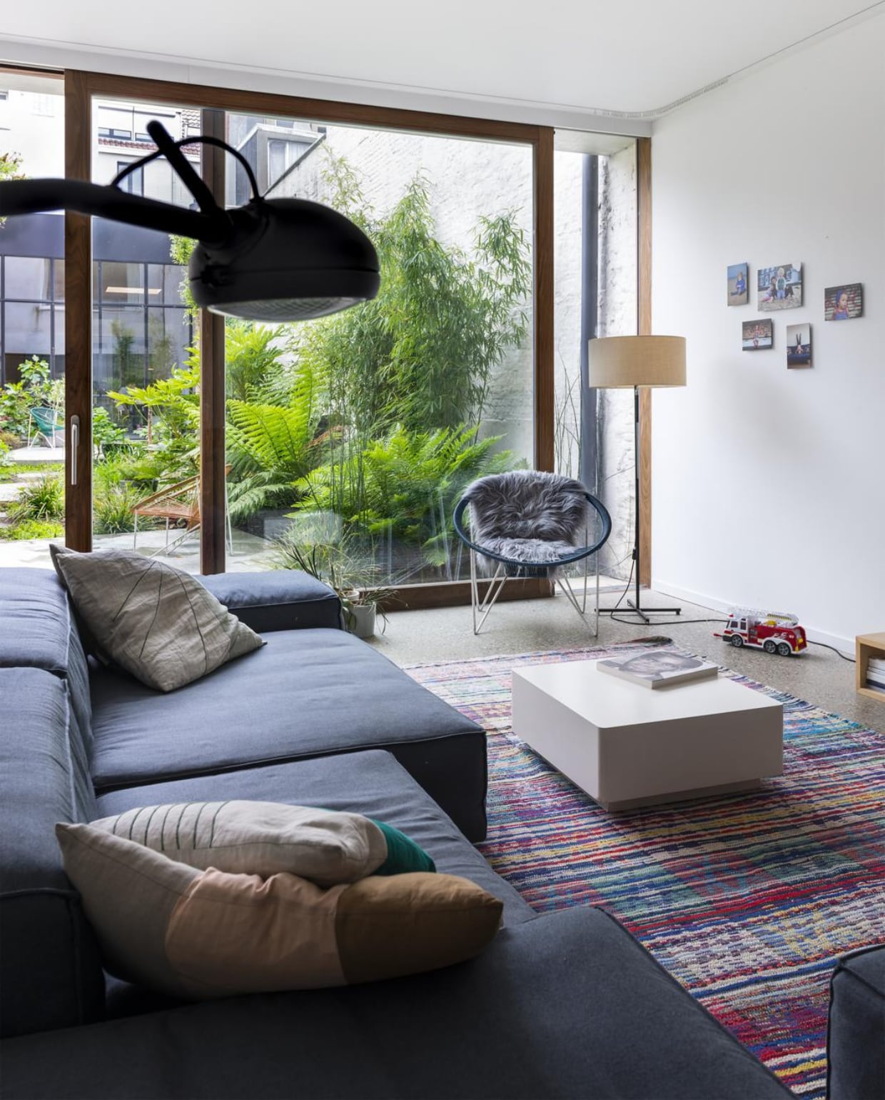 Door in het midden een stuk van de garage af te breken ontstond een stadstuin. Achteraan liet het koppel een stuk van het gebouw staan. Dat is nu een kantoorruimte voor Studio Reset en een logeerkamer. In het salon staat een modulaire zetel van Living Divani, met daarin kussens gemaakt door vriendin en ontwerpster Sarah Patoor. De zwarte booglamp Stand Alone is van Jacco Maris, het tapijt is gekocht in Marokko. In de hoek staat een stoel die het koppel vond bij Modest Furniture en een vintage lamp uit de fifties. De salontafel heeft ooit dienst gedaan als podium voor paspoppen in een winkel, een oud project. vtwonen 10-2017 | Fotografie Stan Koolen