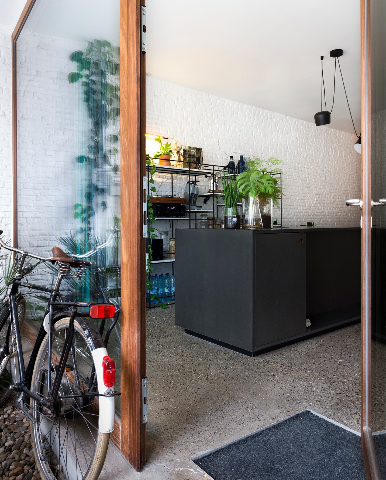 De woning heeft op de benedenverdieping twee voorgevels. De voorste is gemaakt uit strekmetaal, de tweede is van glas. De ruimte ertussen gebruiken Leen en Tim als fietsenstalling en voortuintje. Het kookeiland is gemaakt van zwarte mdf die werd vernist. ‘Op korte termijn maken we dat eiland groter en komt er een nieuw werkblad in roestvrij staal’, zegt Leen. Het asymmetrische wandrek in marmer en staal is een gezamenlijk ontwerp dat het koppel liet maken met restjes marmer. Boven het kookeiland hangen Aim lampen van Flos. vtwonen 10-2017 | Fotografie Stan Koolen