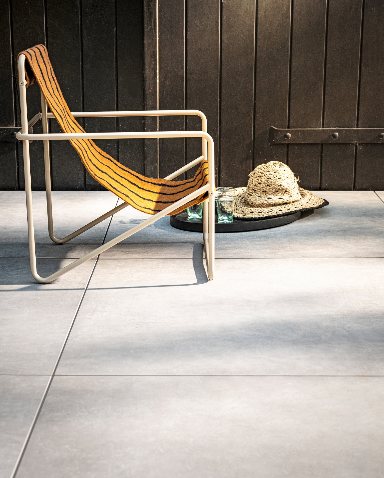 Tegel Solostone Uni Mold Grit, , 90x90x3 cm (lxbxh) per m² € 80,- (ook verkrijgbaar in Basalt, en in Grit, Basalt en Taupe in 70x70x3,2 cm). M.m.v. kolkenkolk.nl (Desert Lounge Chair kids van Ferm Living), vtwonen.nl (dienblad van Serax), householdhardware.nl (glazen). Overig privébezit.