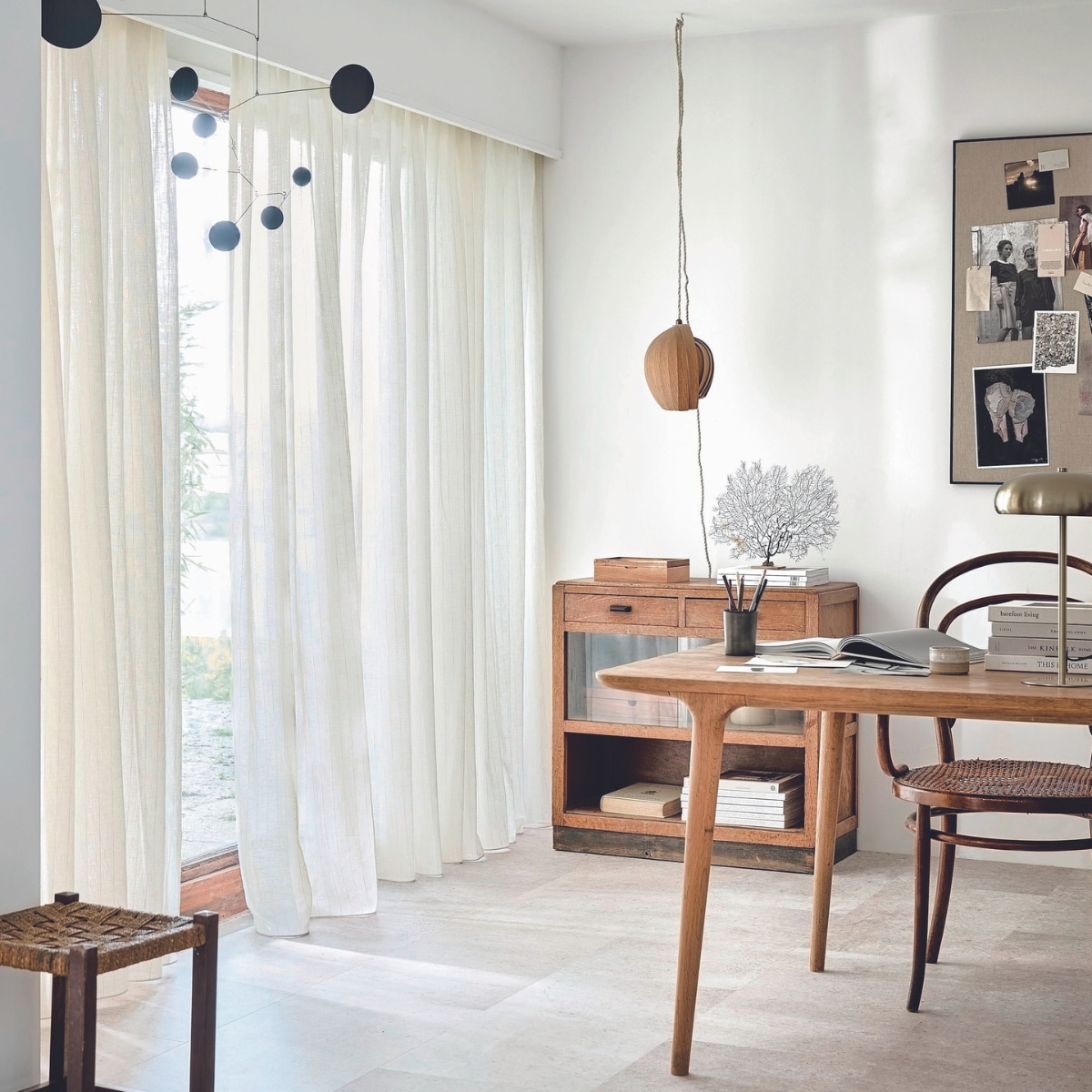 Inbetween transparant gordijn op maat in stof Wide Stripes, kleur Ecru White Stripe (2316), per meter vanaf € 27,99.M.m.v. kringloop (kruk, kast), zarahome.com (prikbord, tafellamp, pennenbak), demuseumwinkel.com (zeewaaier), moduleo.com (vloer), lpln.de (mobile). vtwonen 08-2024 | styling Kim van Rossenberg | fotografie Sjoerd Eickmans