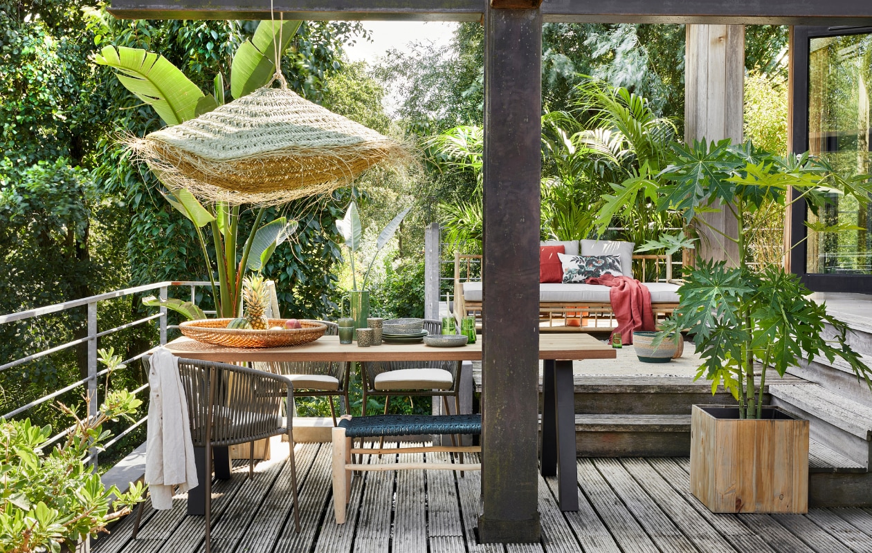 Outdoor eettafel Tablo met A-poot van metaal € 599,- (woood.nl). Tuinstoelen  Yanet van Kave Home, per stuk € 128,40, bamboe daybed van Exotan € 579,-, houten plantenbak Marrone Cube L € 112,99 (vtwonen.nl). Bank met groene macramé zitting, prijs op aanvraag, grijs-groene mand Nile, per set van 2 € 55,-, vloerkleed Wabi Sabi, 150x220 cm € 249,- (zenzahome.com). Grote bamboe schaal € 44,95, grijze borden Odile, per set van vier € 37,95 (loods5.nl). Gevlochten hanglamp € 149,50 (householdhardware.nl). Groene mokken 70’s Grass, per stuk € 6,75, groene borden 70’s, per stuk € 27,95, gebloemd kussen Kyoto € 24,95 (hkliving.nl). Groen conisch glas, per stuk  € 4,50 (householdhardware.nl). Steenrood linnen kussen Vigdis € 6,99, steenrood linnen doek Dytag € 59,99 (ikea.nl).