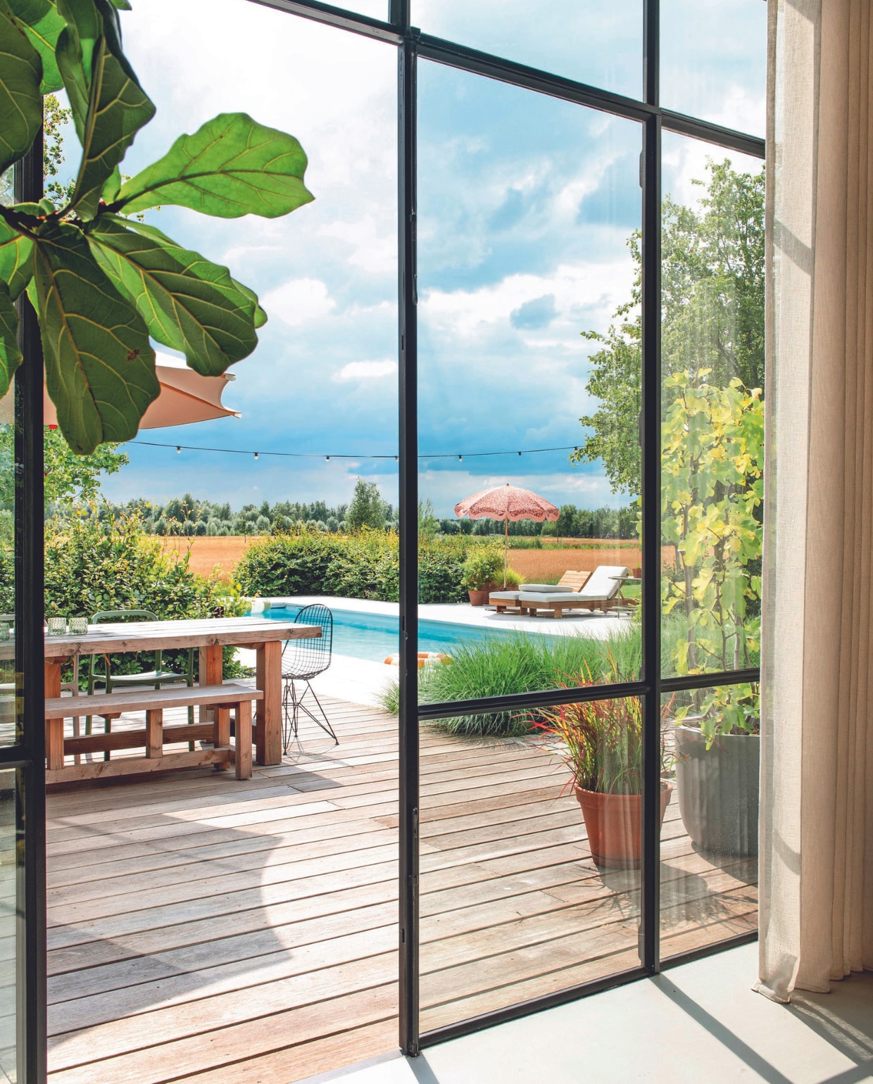 Houten tuintafel Marktplaats, stoel Vitra, kleine parasol HKliving, ligbedden Wehkamp. vtwonen 08-2024 | styling Jeske Weel | fotografie Caroline Coehorst