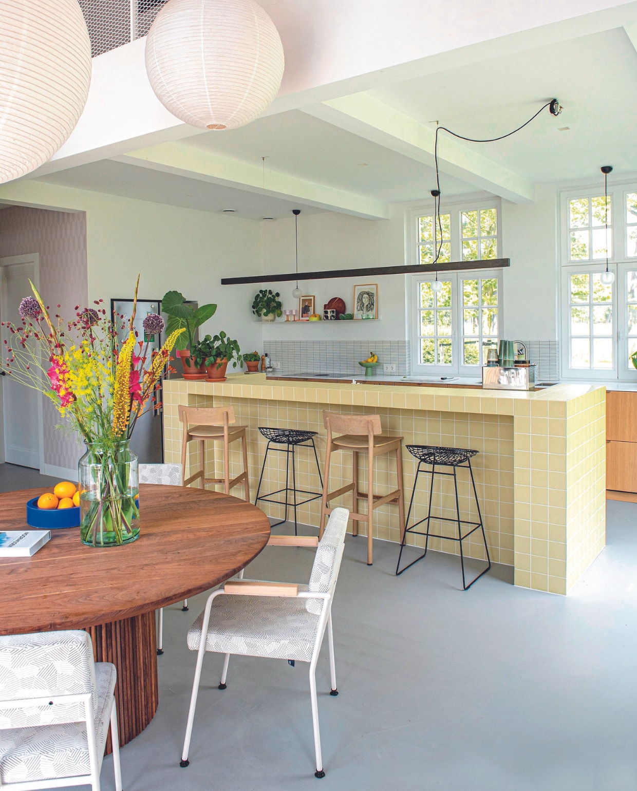 Behang Arte. Keuken Van den Berg Keukens, keukenbar Winckelmans, zwarte barkrukken Wire van Pastoe, houten barkrukken Woud, hanglampen Muuto, koffiemokken en groene fruitschaal HKliving. Eettafel Studio à la part, eetkamerstoelen en blauwe fruitschaal Fést, plafondlampen Hay. vtwonen 08-2024 | styling Jeske Weel | fotografie Caroline Coehorst