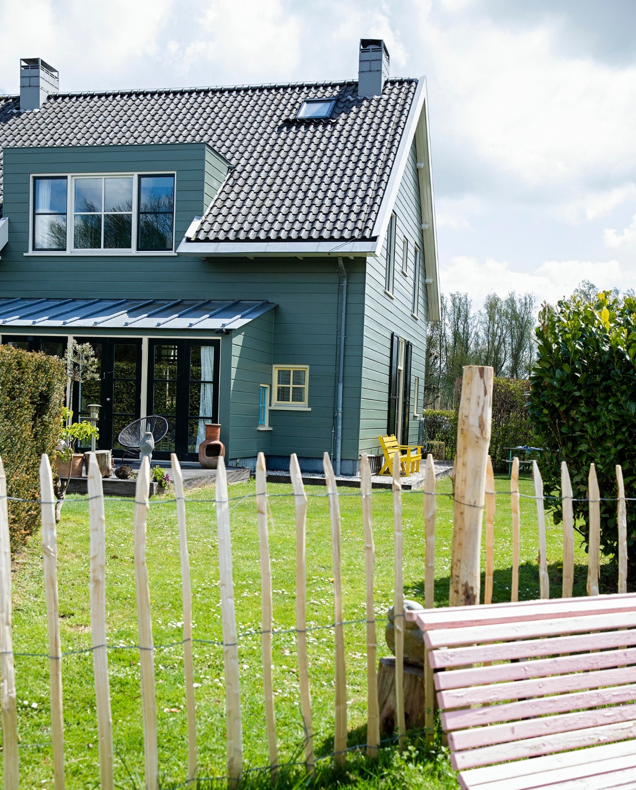 Het huis is aan de buitenkant afgetimmerd met hout, maar heeft een betonnen constructie. De kleur is bepaald door de monumentencommissie en mag niet worden veranderd. Tuinbank van de kringloop geschilderd in Nancy’s Blushes van Farrow &amp; Ball. vtwonen 07-2021 | styling Ilona Jongepier | fotografie Dana van Leeuwen