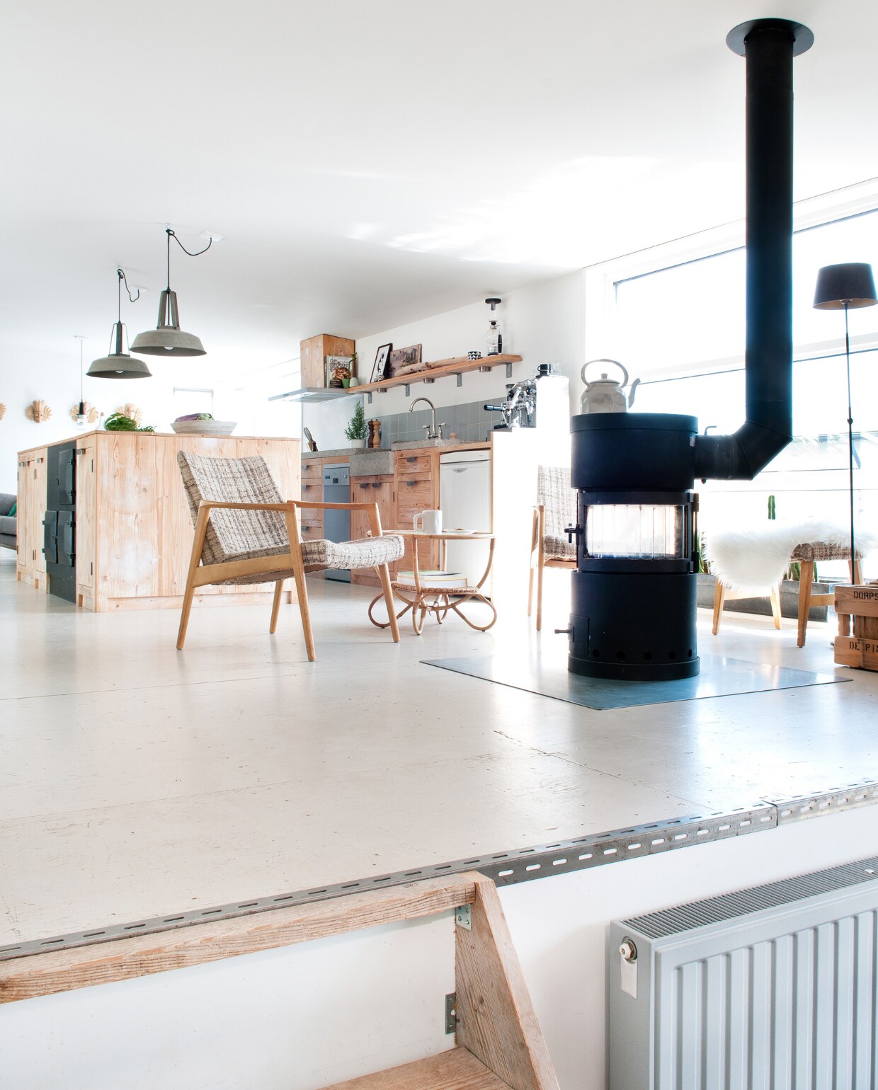 Op de vloer in de eethoek liggen steigerhouten planken. Van steigerhout is ook het kastje naast het trapgat. ’Het staat er als bescherming. Er komen hier ook kinderen, en het is een aardige val.’ Het kunstwerk is van Paul Jansen, een houtbewerker (www.totempauljansen.nl). Omdat bezoekers het kunstwerk gebruiken als trapleuning, is hij vanuit de kelder vastgezet. De radiator rechts van het trappetje is nieuw, maar – net als alle andere radiatoren - zo veel mogelijk industrieel gemaakt met de leiding aan de buitenkant, een metalen knop en grijze verf. Lampen Nijhof, kachel via Marktplaats, werkeiland gemaakt met oude kaasplanken. Fauteuils van een kringloopwinkel.“We houden van dat rauwe. De metalen profielen langs de vloer mogen worden gezien vtwonen 03-2017 | styling Irene van den Brink | fotografie Suzanne Paap