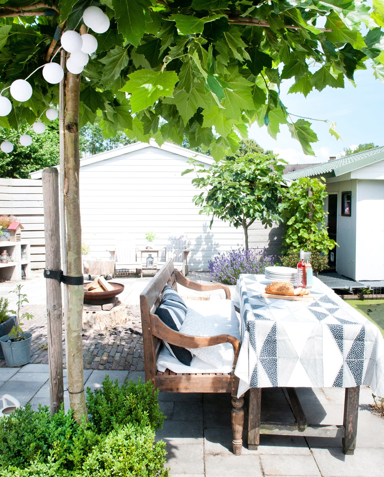 De tuin loopt schuin. Op het breedste punt is hij 19 meter. De teakhouten bank is oorspronkelijk een Indonesische stationsbank. ’s Winters staat-ie binnen bij de eettafel. Kussen Ikea, vuurschaal op de achtergrond Nijhof. vtwonen 03-2017 | styling Irene van den Brink | fotografie Suzanne Paap