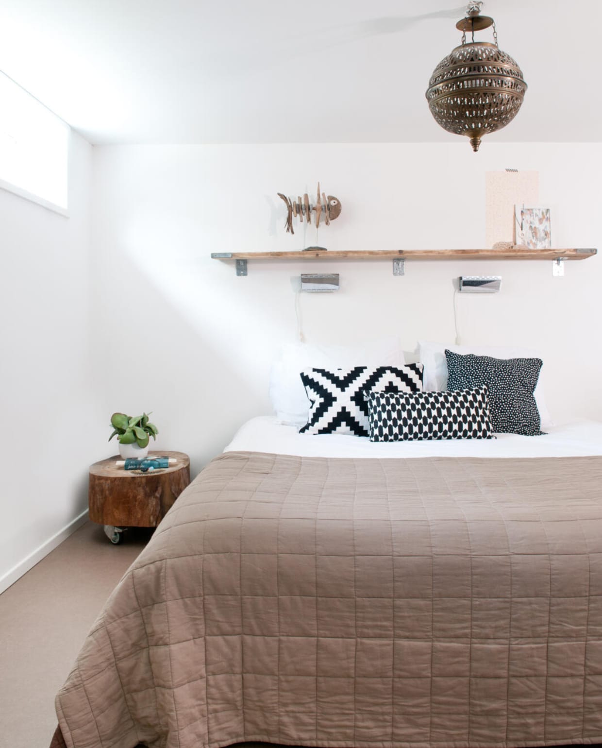 Naast de badkamer is de slaapkamer. Op de vloer ligt vinyl. Het tafeltje is gemaakt van een treurwilg uit de tuin. Wielen eronder, klaar. De lamp komt uit Marokko, de vis op de steigerhouten plank is gemaakt door houtbewerker Marcel Dijker (www.dijkstijl.com). Sprei, kussens en bedlampjes Ikea. vtwonen 03-2017 | styling Irene van den Brink | fotografie Suzanne Paap