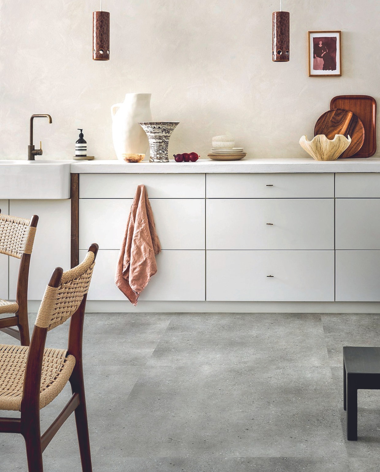 Pvc-vloer Composite XL in Warm Grey, 91,4x91,4 cm, dryback per m² € 42,95.M.m.v. wearewowmakers.com (muurverf Mykonos), vtwonen.nl/shop (stoelen van Dutchbone, vaas, servies van By Fonq), urbannatureculture.com (witte kan, geschulpte schaal), tinystories.nl (print), hkliving.com (hanglampen), sissy-boy.com (schaaltje marmereffect), skins.nl (handzeep Aesop). vtwonen 08-2024 | styling Marlies Does | fotografie Sjoerd Eickmans